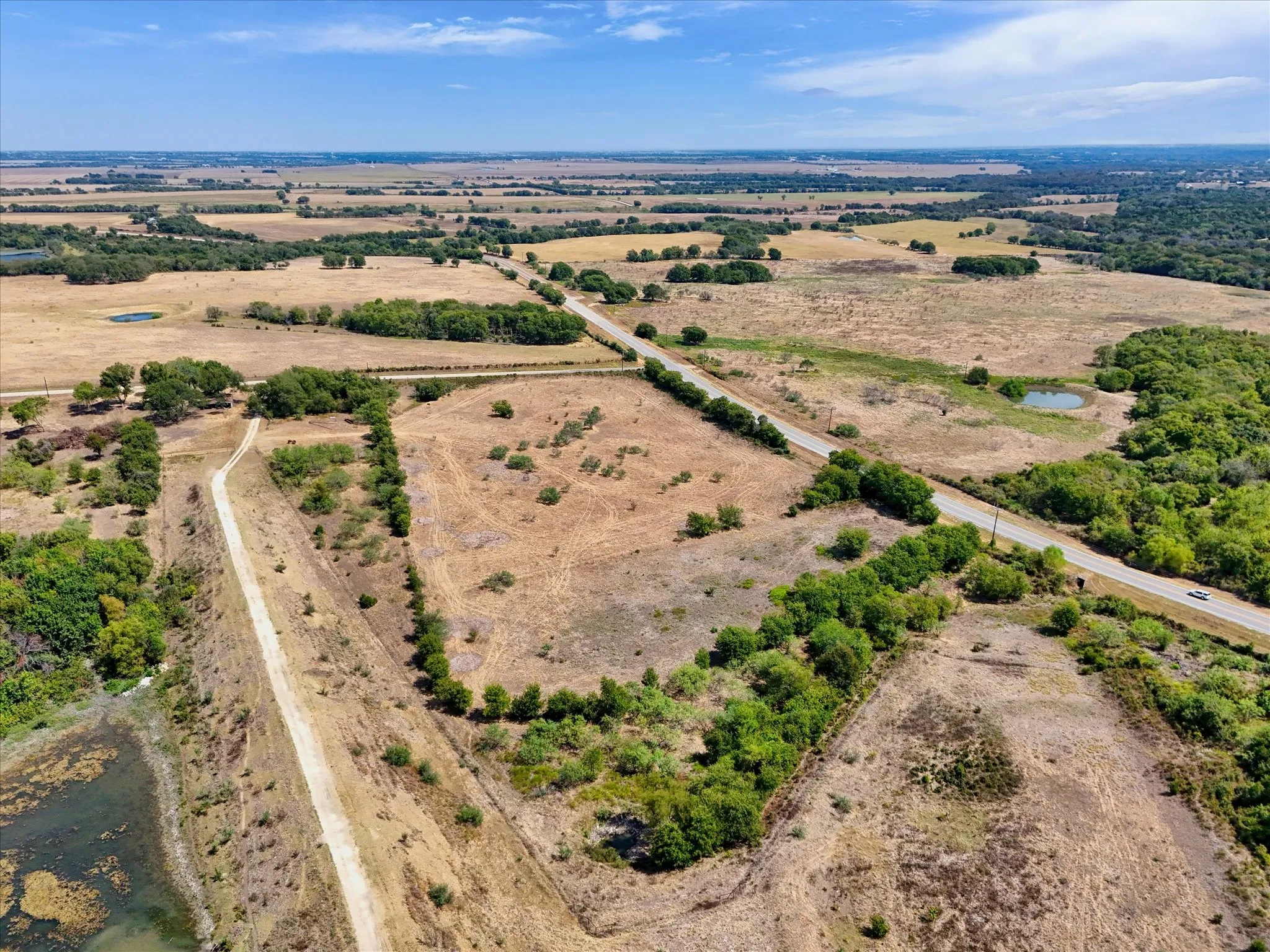 Expansive land parcels with scattered trees, a paved road, and a water feature