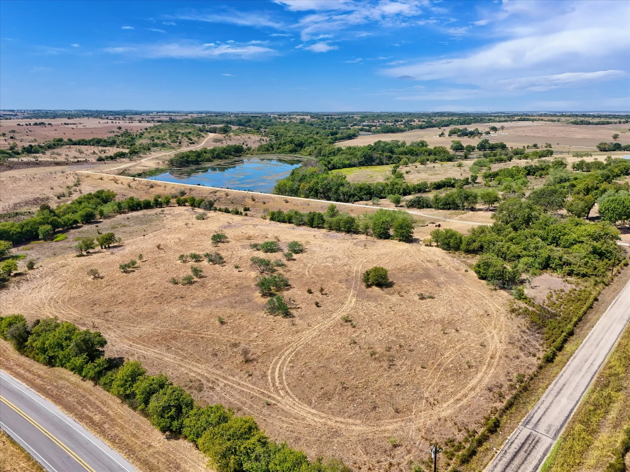 Expansive land featuring a natural pond, scattered mature trees, and direct road frontage