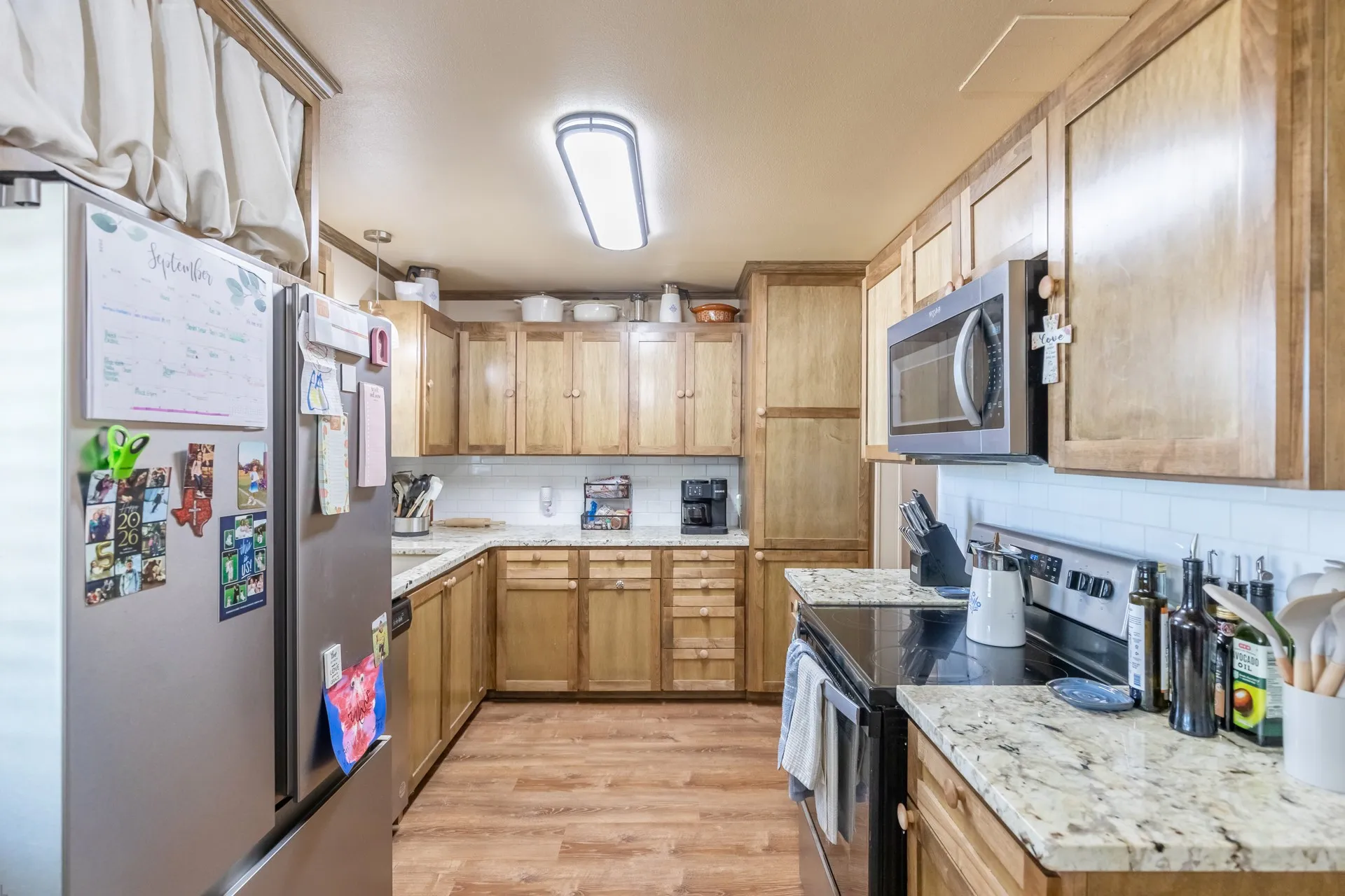 Wood-finish flooring, light wood cabinetry, white subway tile backsplash, light-toned countertops, and a built-in microwave