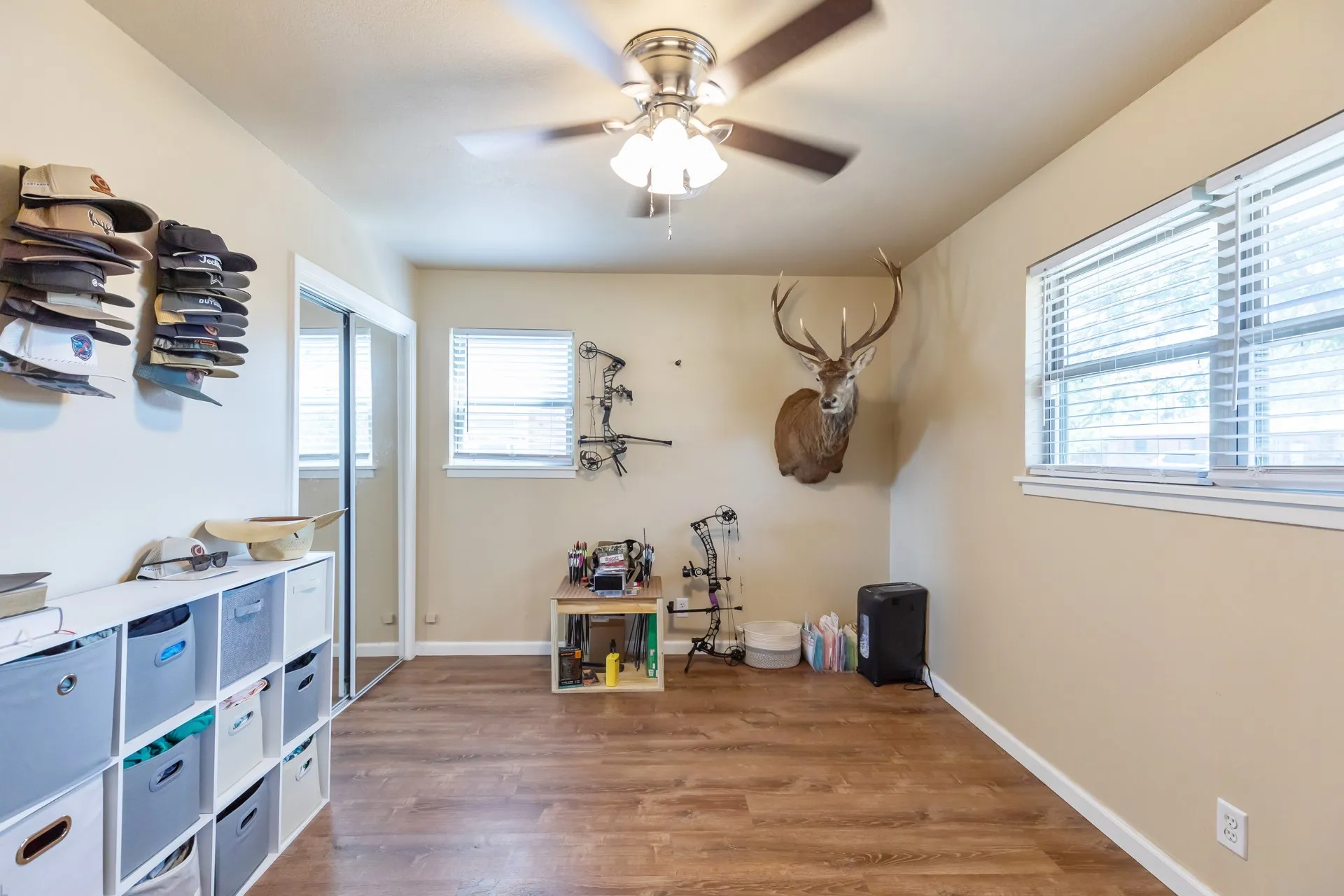Wood-finish flooring, ceiling fan with integrated lighting, and two windows with blinds