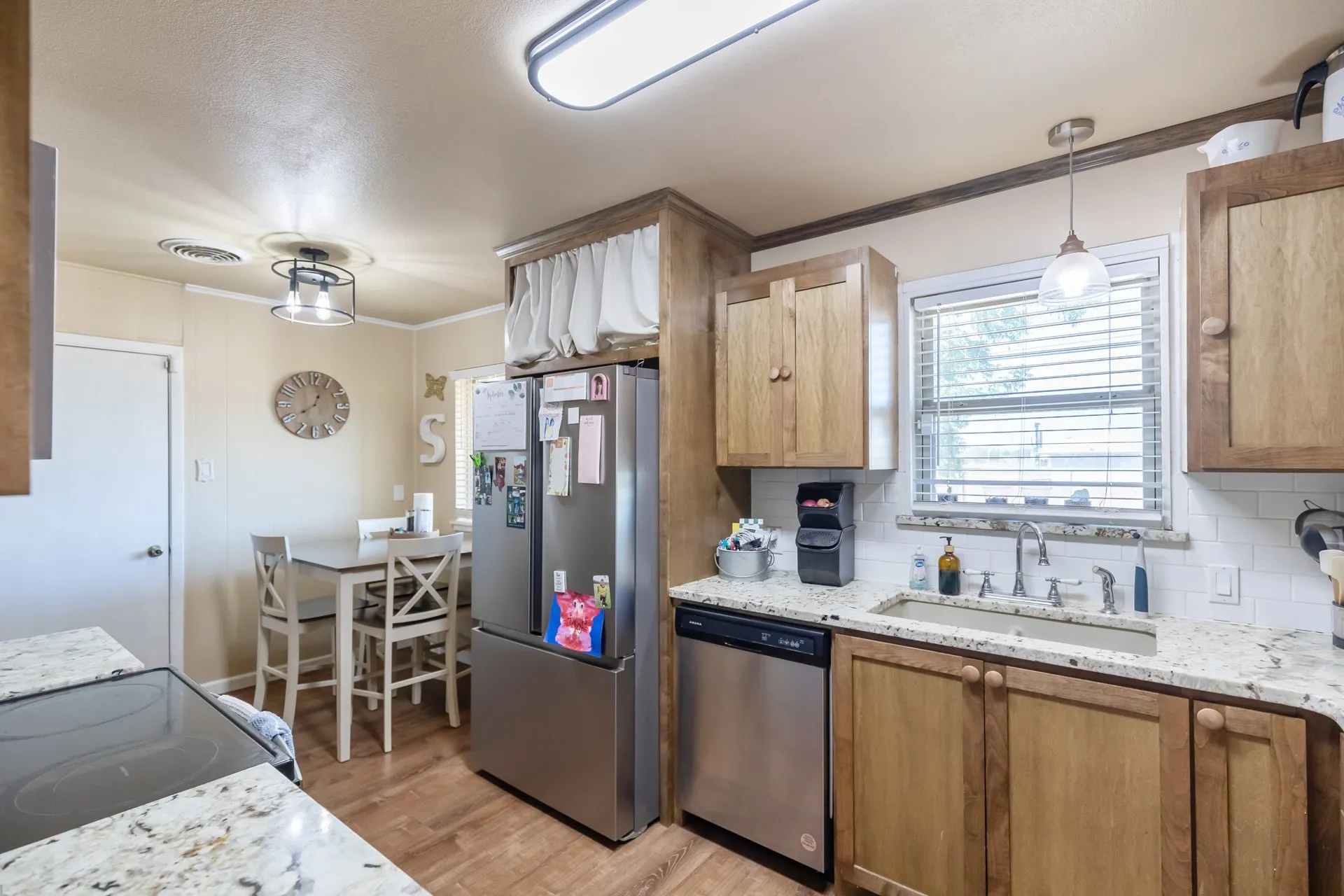 Wood-finish cabinetry, stainless steel appliances, granite-finish countertops, wood-finish flooring, and white subway tile backsplash