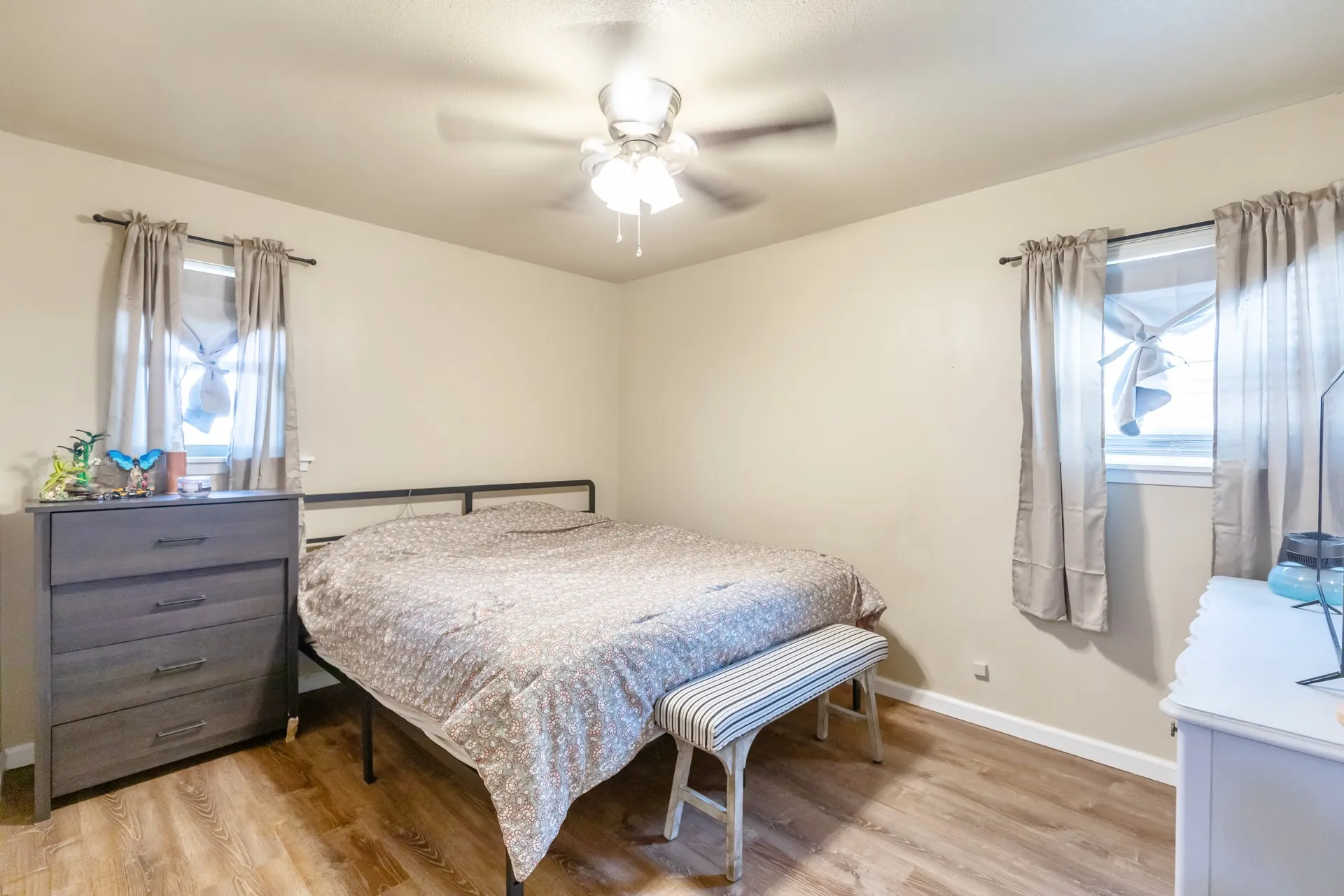 Room featuring wood-finish flooring, a ceiling fan with integrated lighting, and two windows with curtain rods
