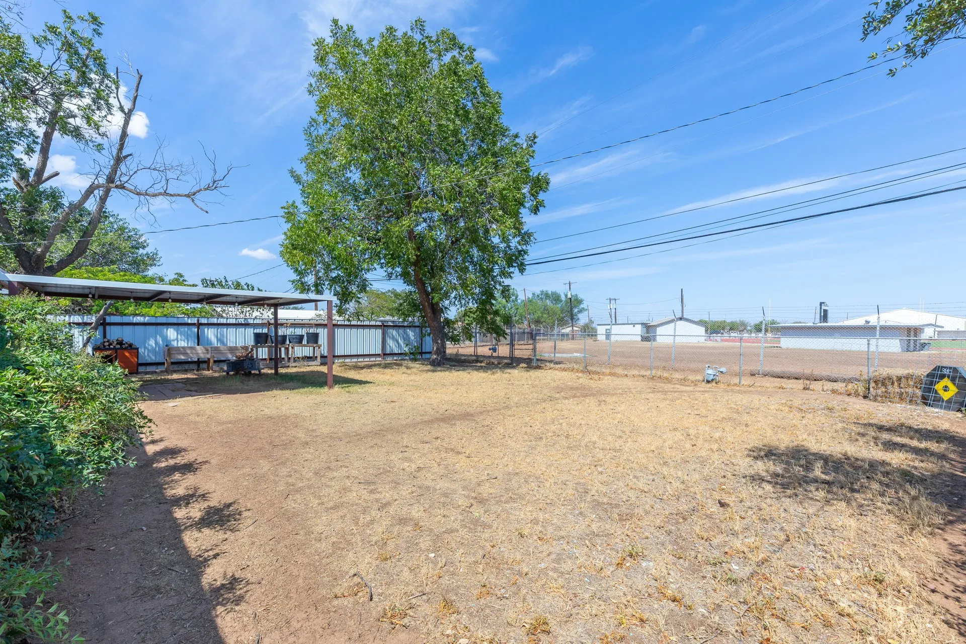 Expansive outdoor space featuring a metal privacy fence, mature trees, and a covered patio area