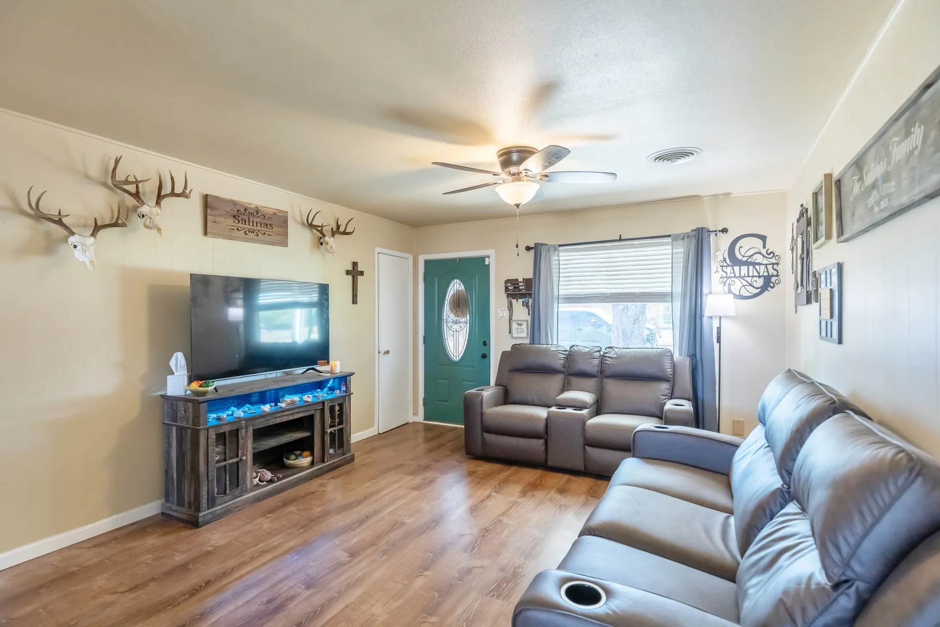 Wood-finish flooring throughout, ceiling fan with integrated lighting, and a window with blinds and drapes