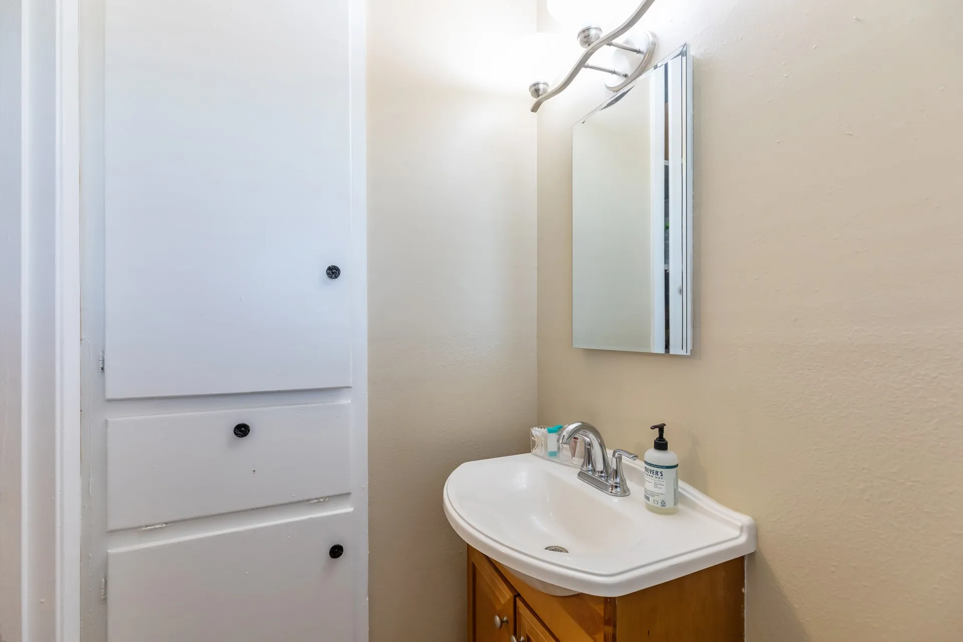 Built-in white cabinetry, corner vanity with integrated sink, wood-finish vanity base, and wall-mounted medicine cabinet with overhead lighting