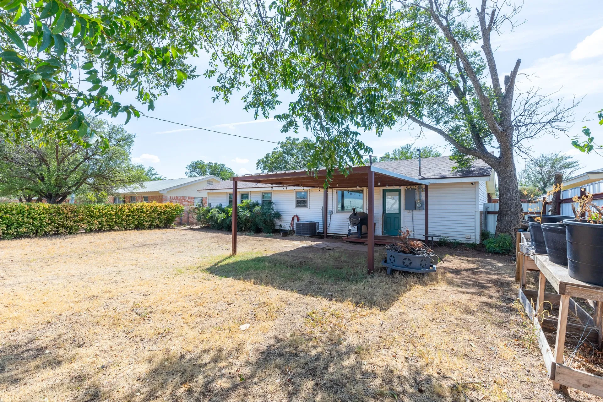Expansive rear yard with a covered patio, mature shade tree, and wood fence