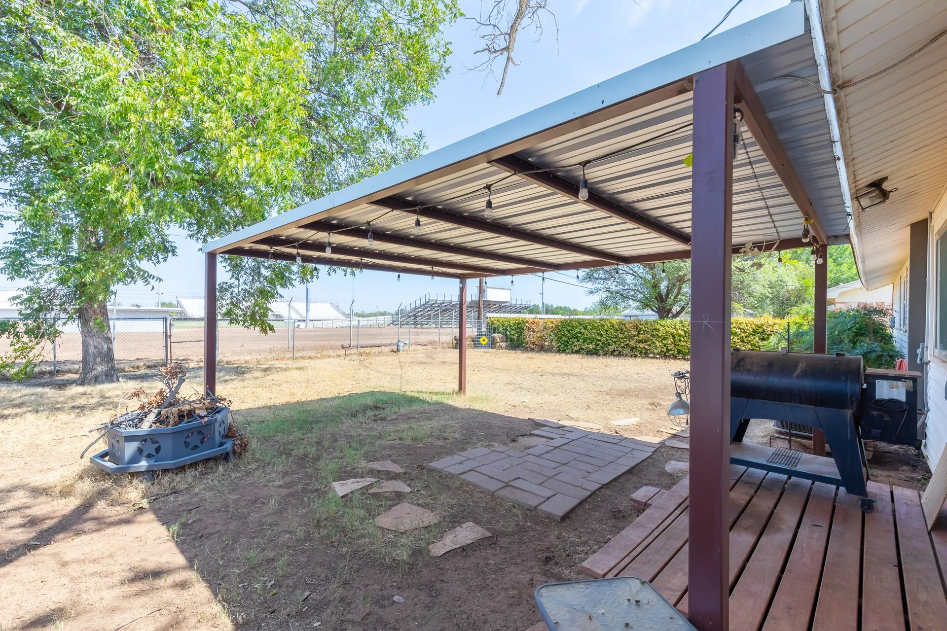 Covered patio with string lights, wood plank decking, and a metal roof structure