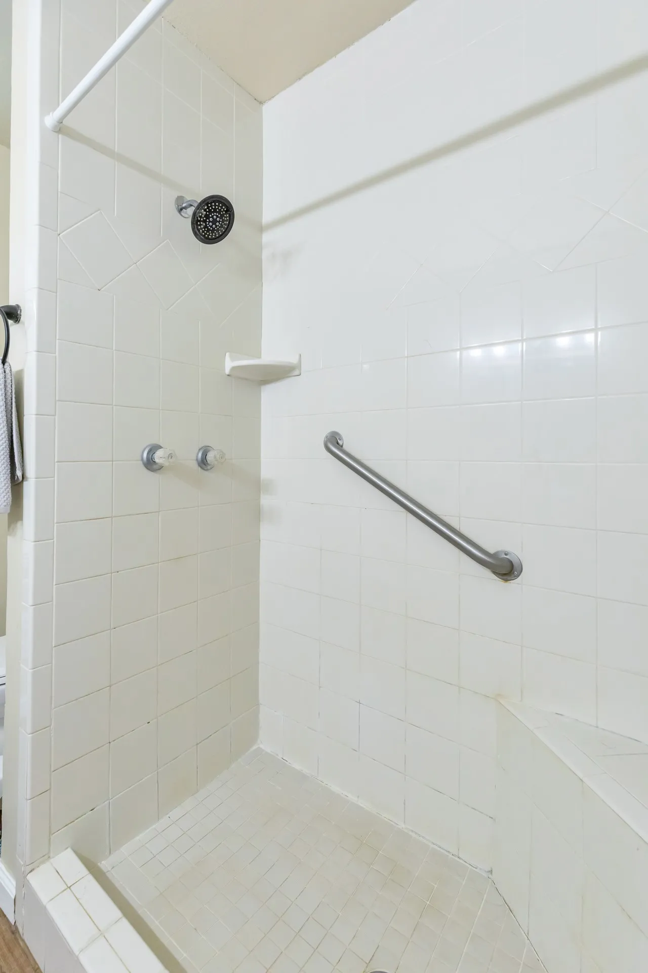 Tile shower with integrated bench seating, wall-mounted showerhead, and grab bar