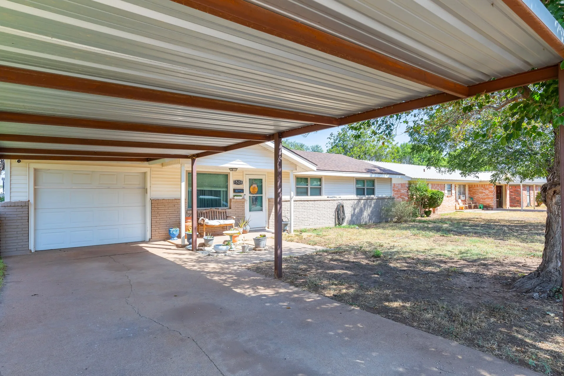 Carport structure over a concrete driveway, featuring an attached single-car garage and a front entrance