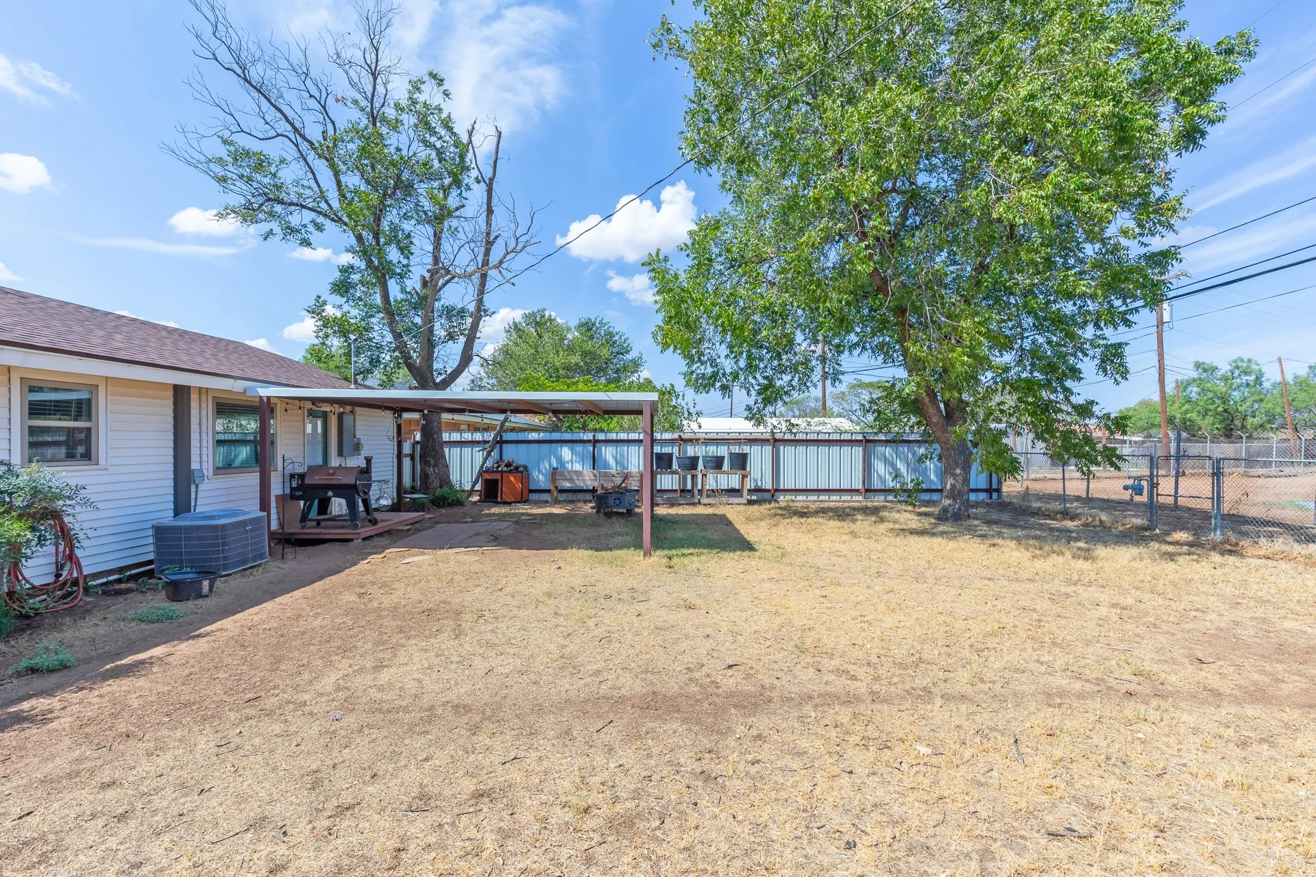 Expansive outdoor space featuring a covered patio, a fully fenced perimeter, and mature trees