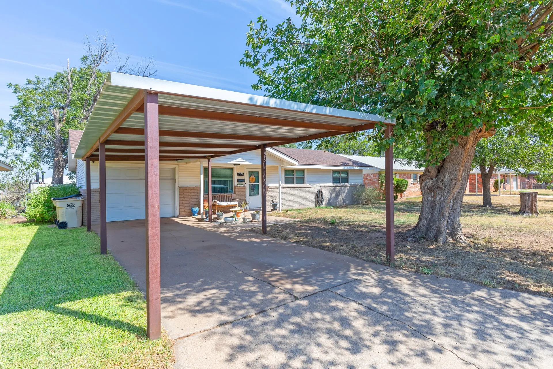 Carport with metal roof and support beams, concrete driveway, attached garage, and a mature tree