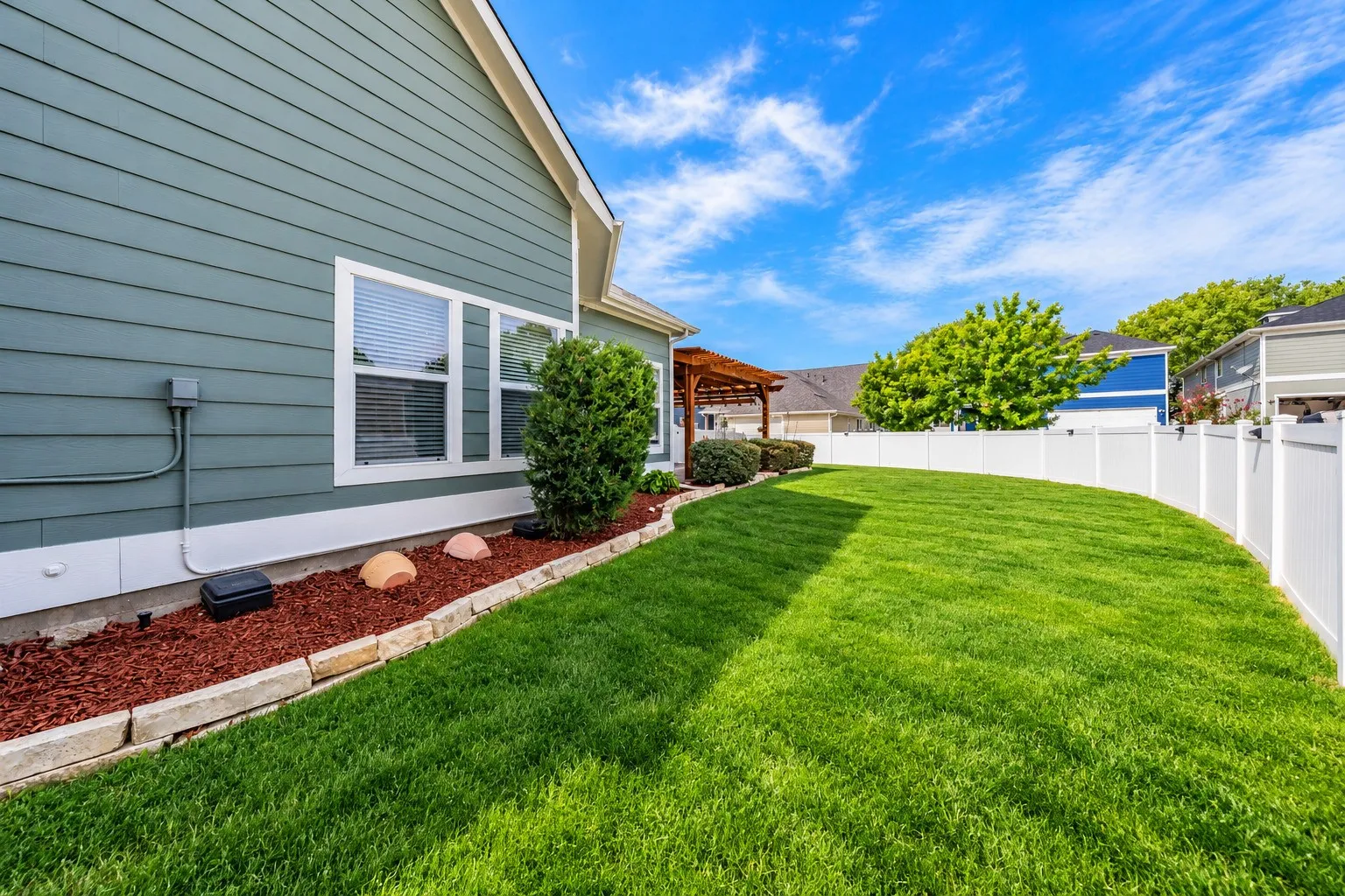Expansive lawn area, white privacy fencing, exterior siding, foundational landscaping, and a visible pergola structure