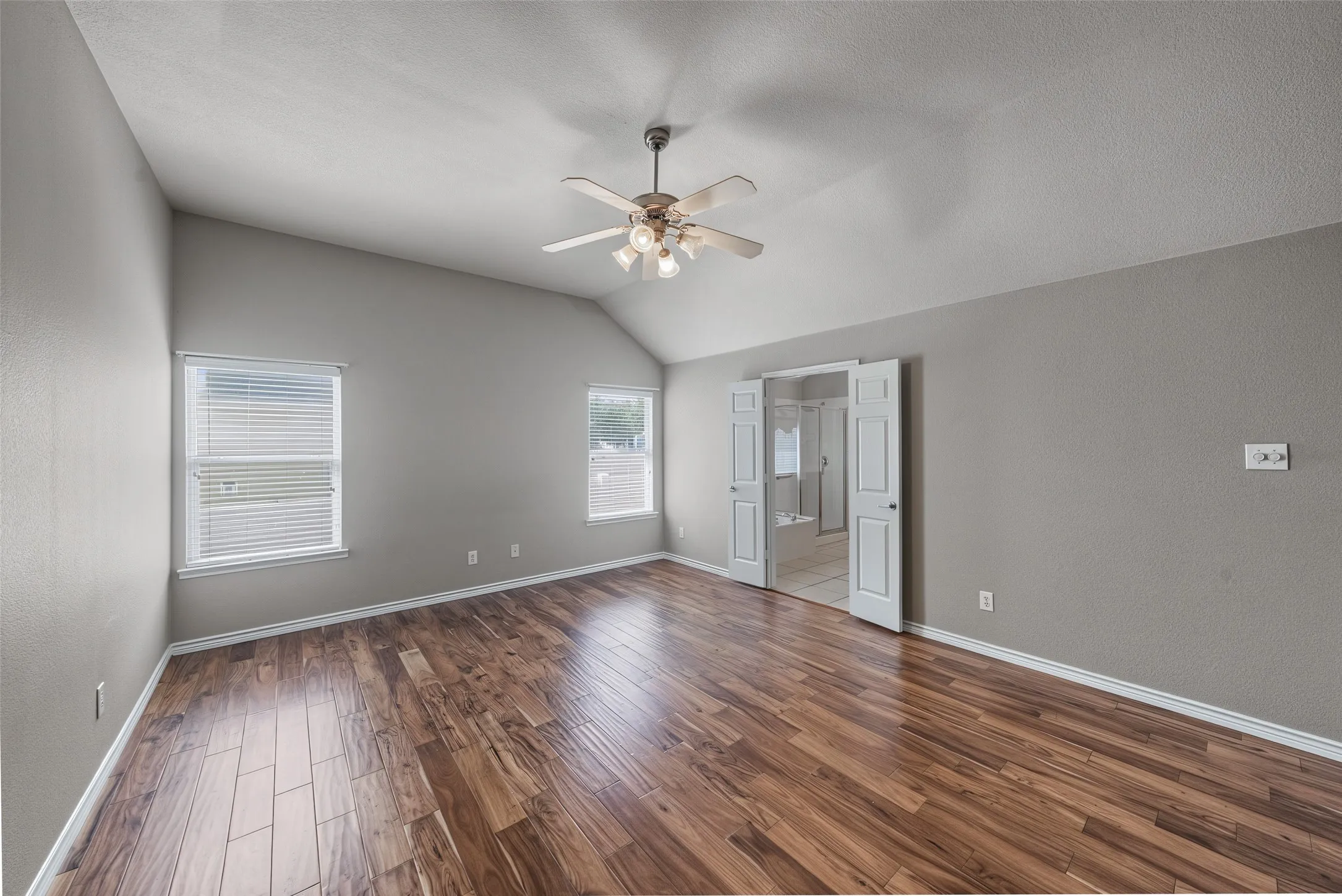 Vaulted ceiling with a ceiling fan, wood-finish flooring, and multiple windows