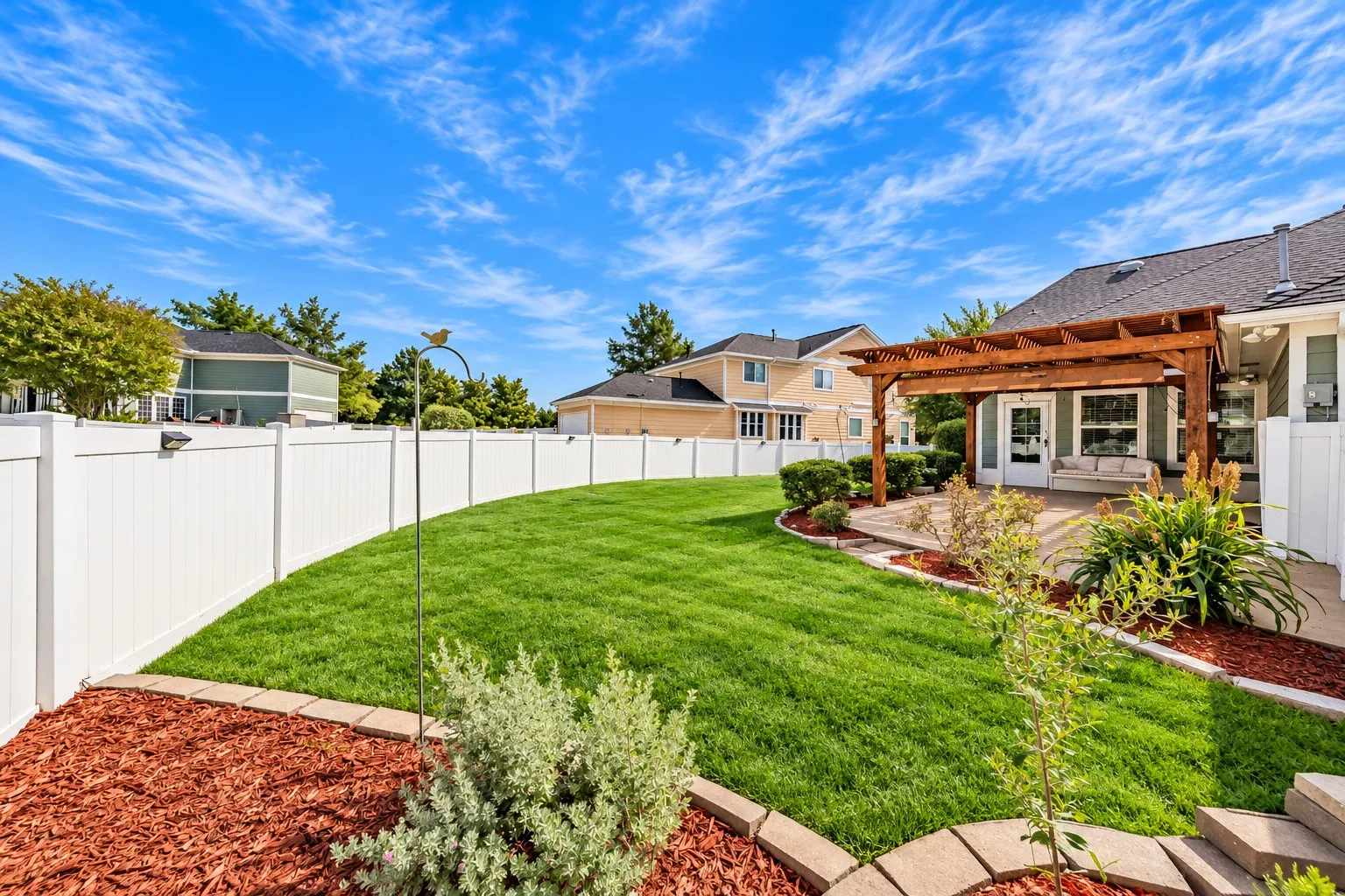 Expansive backyard featuring a manicured lawn, white privacy fencing, a wood pergola, and a stone patio