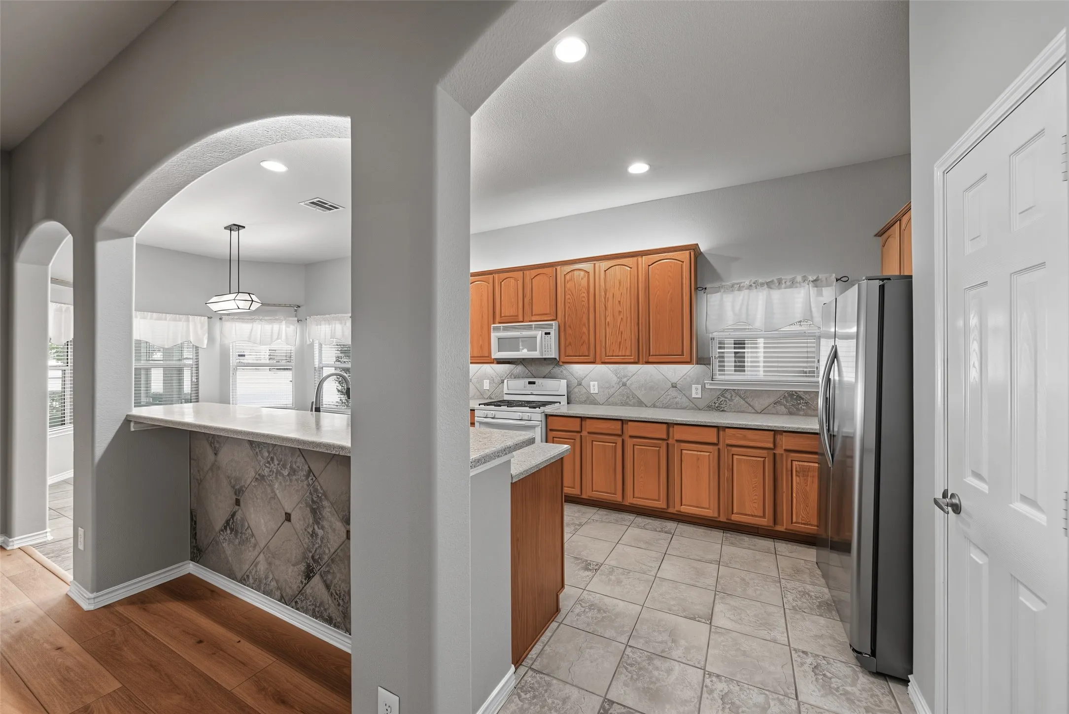 Kitchen featuring wood-finish cabinetry, stainless steel appliances, light-toned countertops, and a tile backsplash