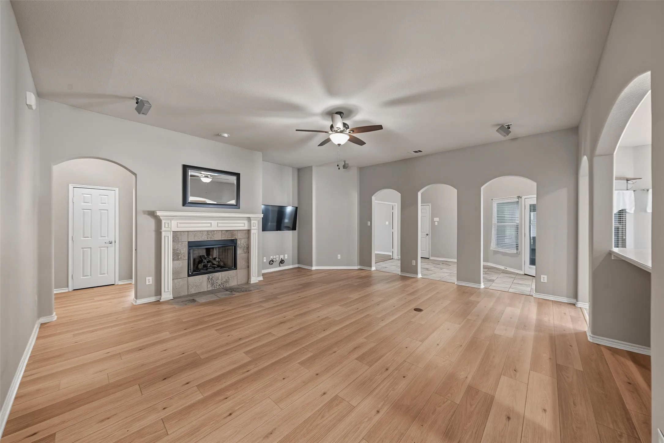 Expansive living area featuring light wood-finish flooring, a central fireplace with a tile surround and decorative mantel, and multiple arched doorways