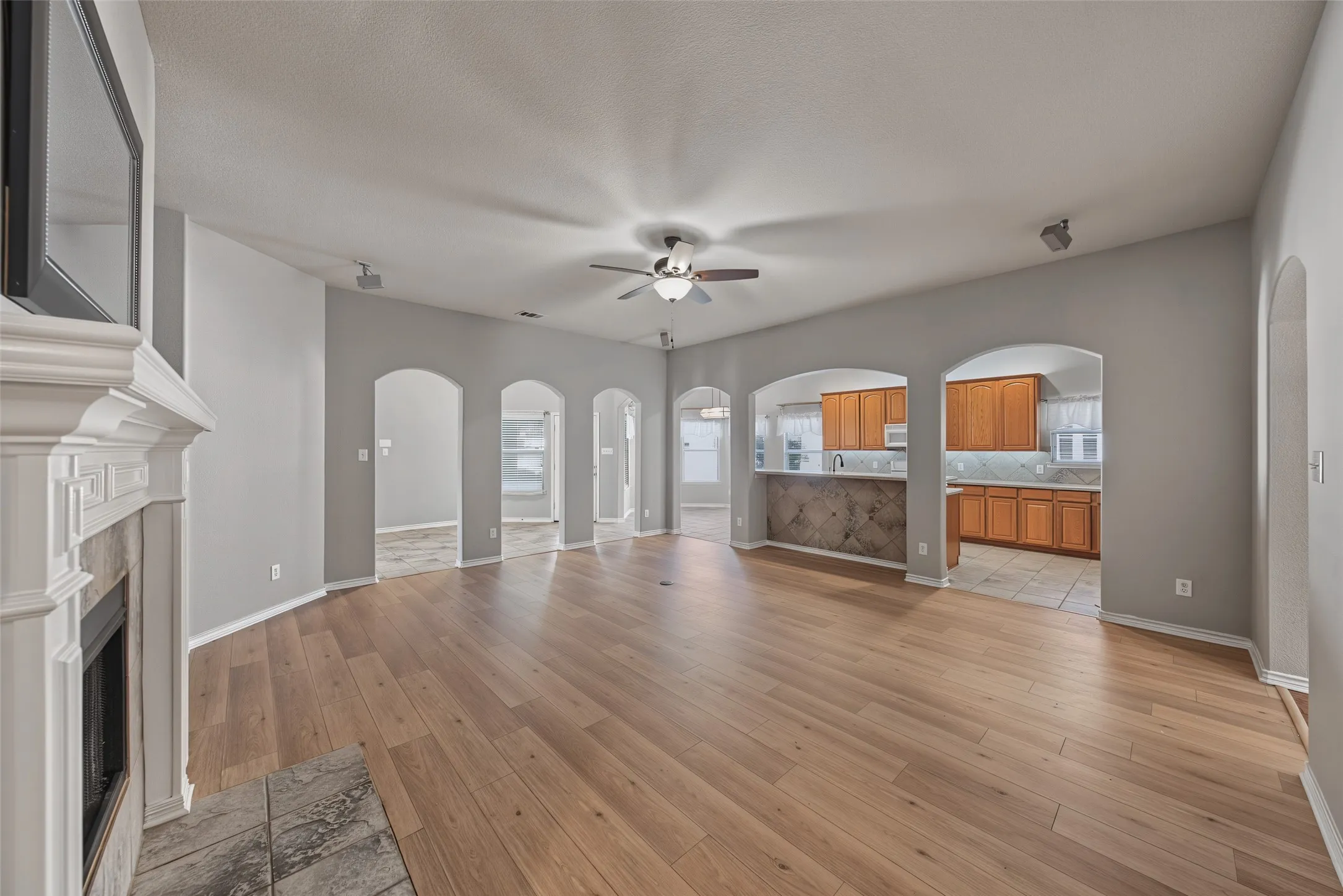 Spacious living area featuring wood-finish flooring, a fireplace with a decorative mantel, vaulted ceilings, and arched doorways