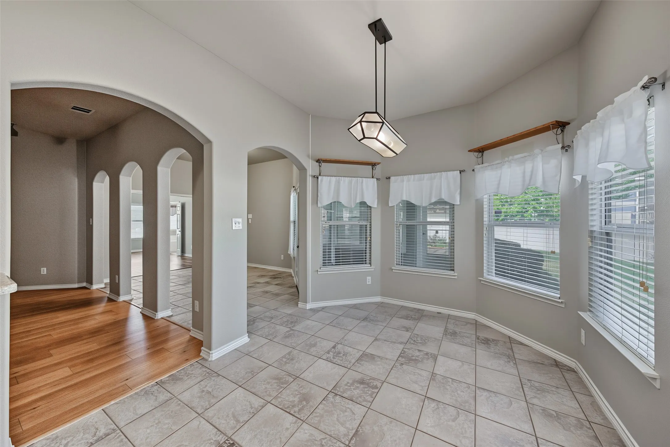 Bay window with multiple panels, tiled flooring, wood-finish flooring, recessed lighting, and arched doorways