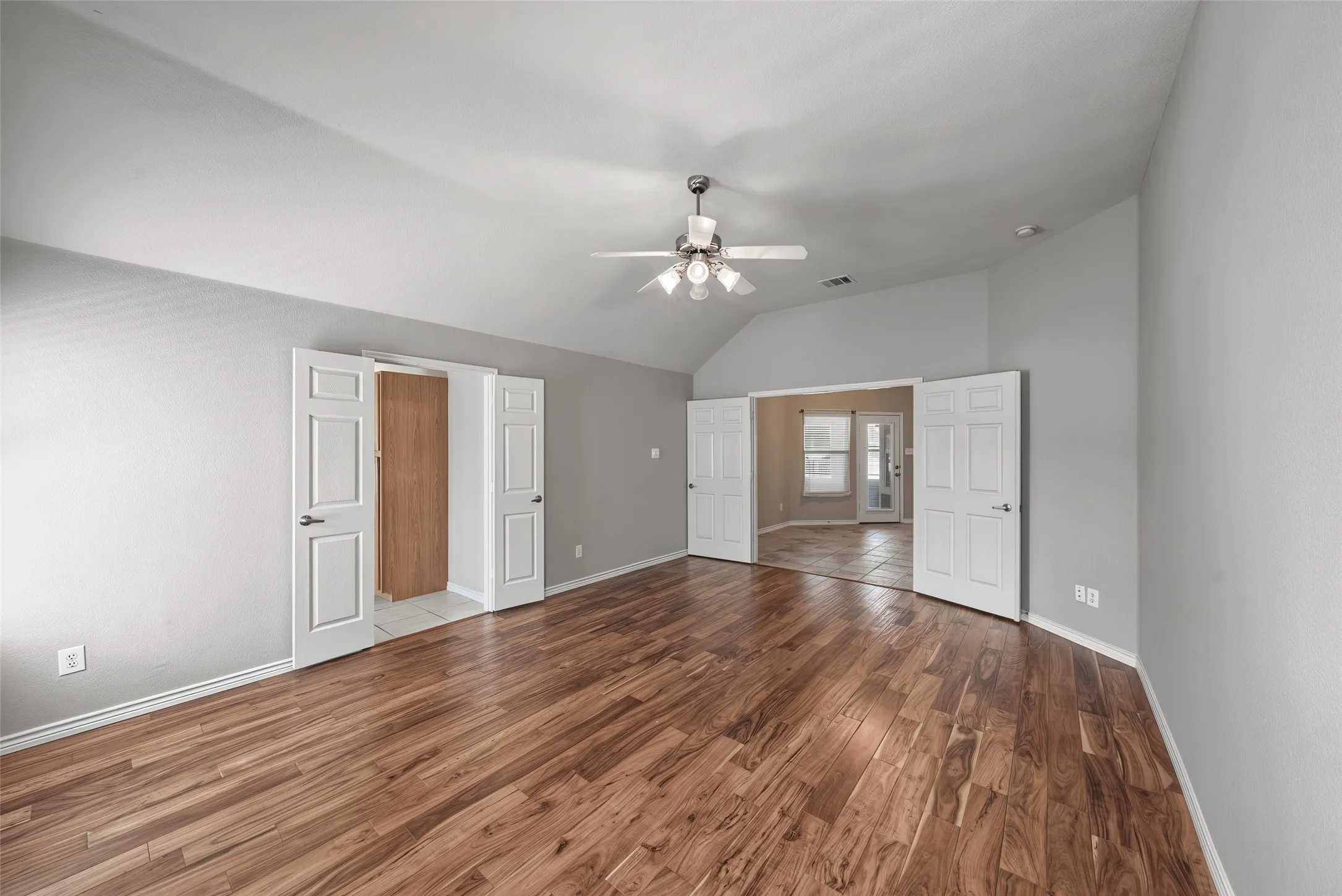 Vaulted ceiling with a ceiling fan, wood-finish flooring, light gray wall paint, and white trim