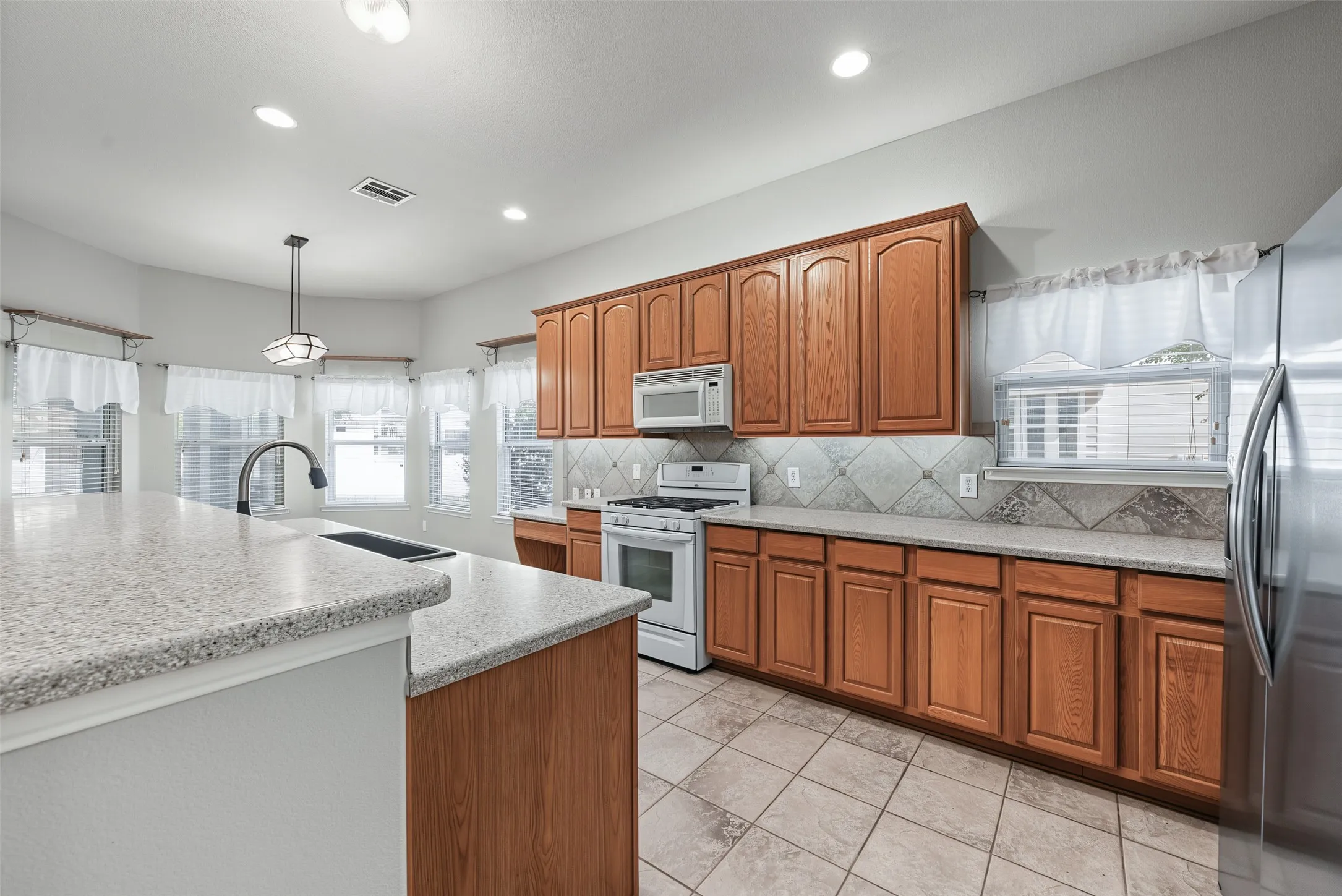 Kitchen featuring wood cabinetry, light countertops, integrated stainless steel refrigerator, white range, and a tiled backsplash