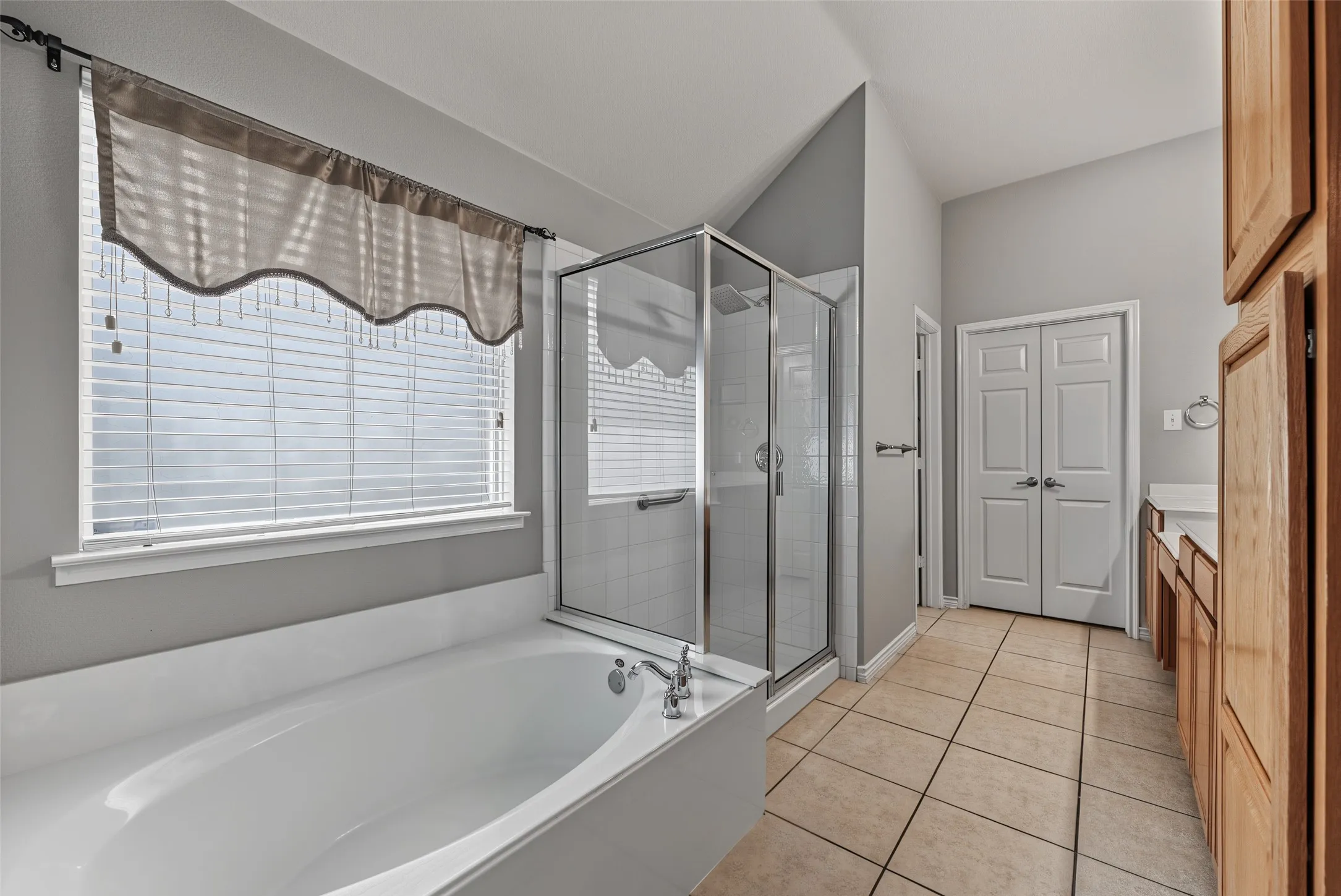 White soaking tub with chrome fixtures, glass-enclosed shower, wood cabinetry, and tile flooring