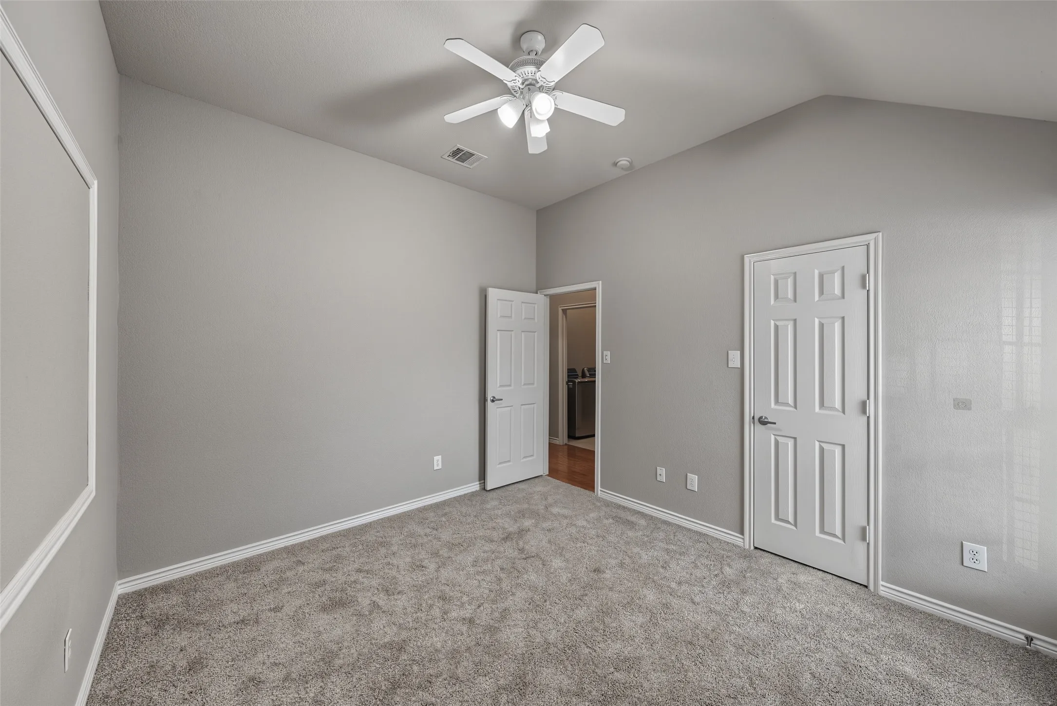 Vaulted ceiling, ceiling fan with light fixture, gray carpet, paneled interior doors, and neutral wall tones