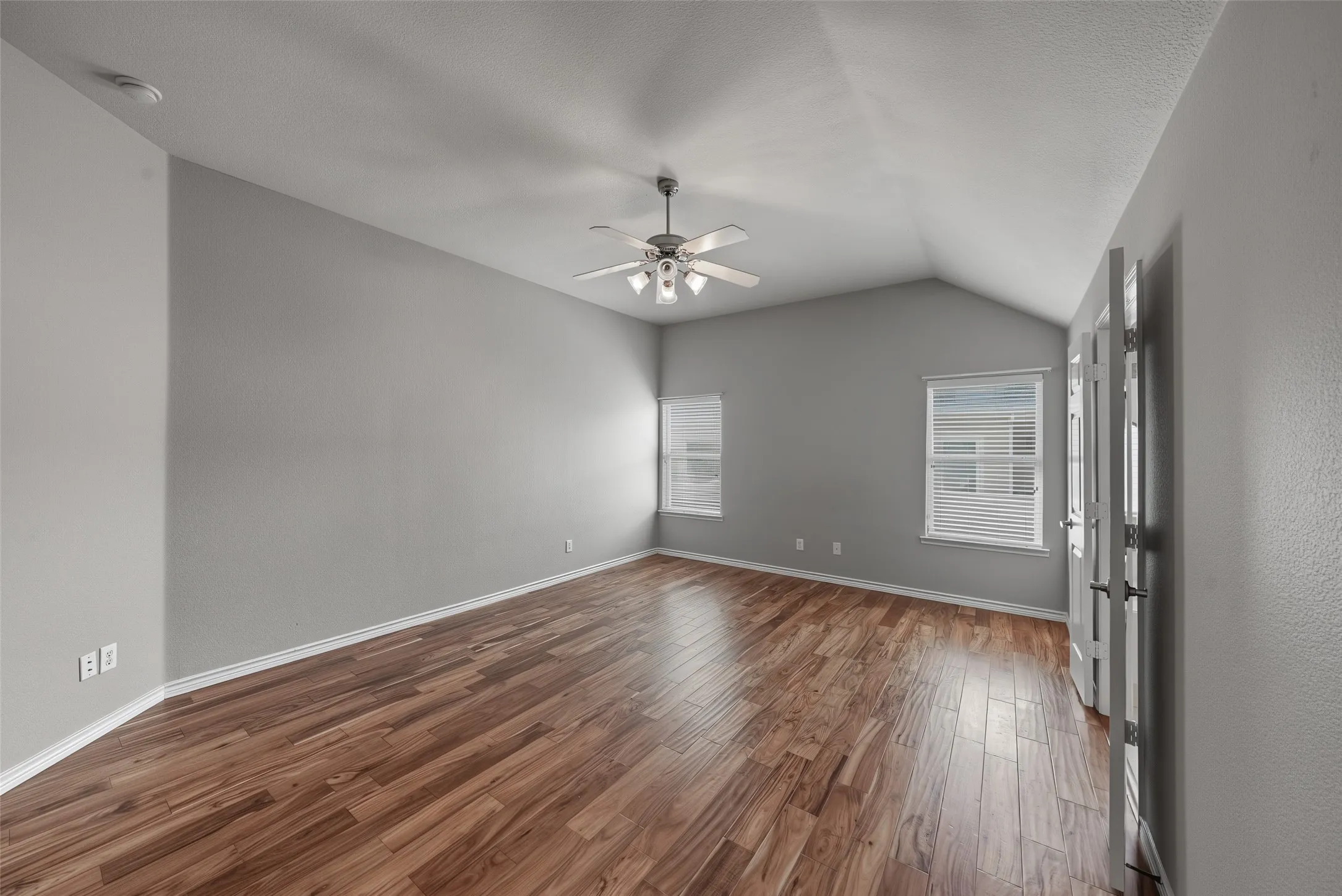 Vaulted ceiling with a ceiling fan, wood-finish flooring, and multiple windows with blinds