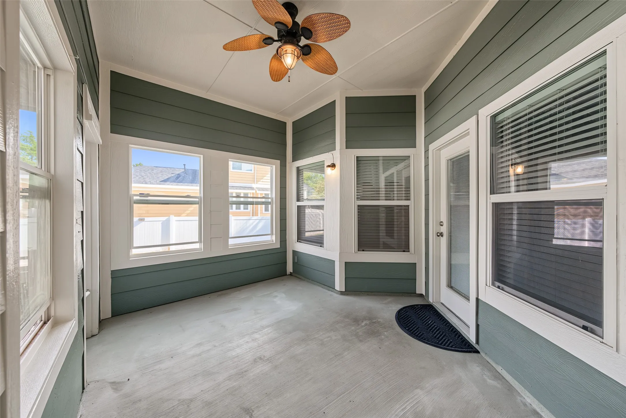 Screened porch featuring green horizontal siding, multiple white-framed windows, a white door, a ceiling fan, and a light-colored concrete floor