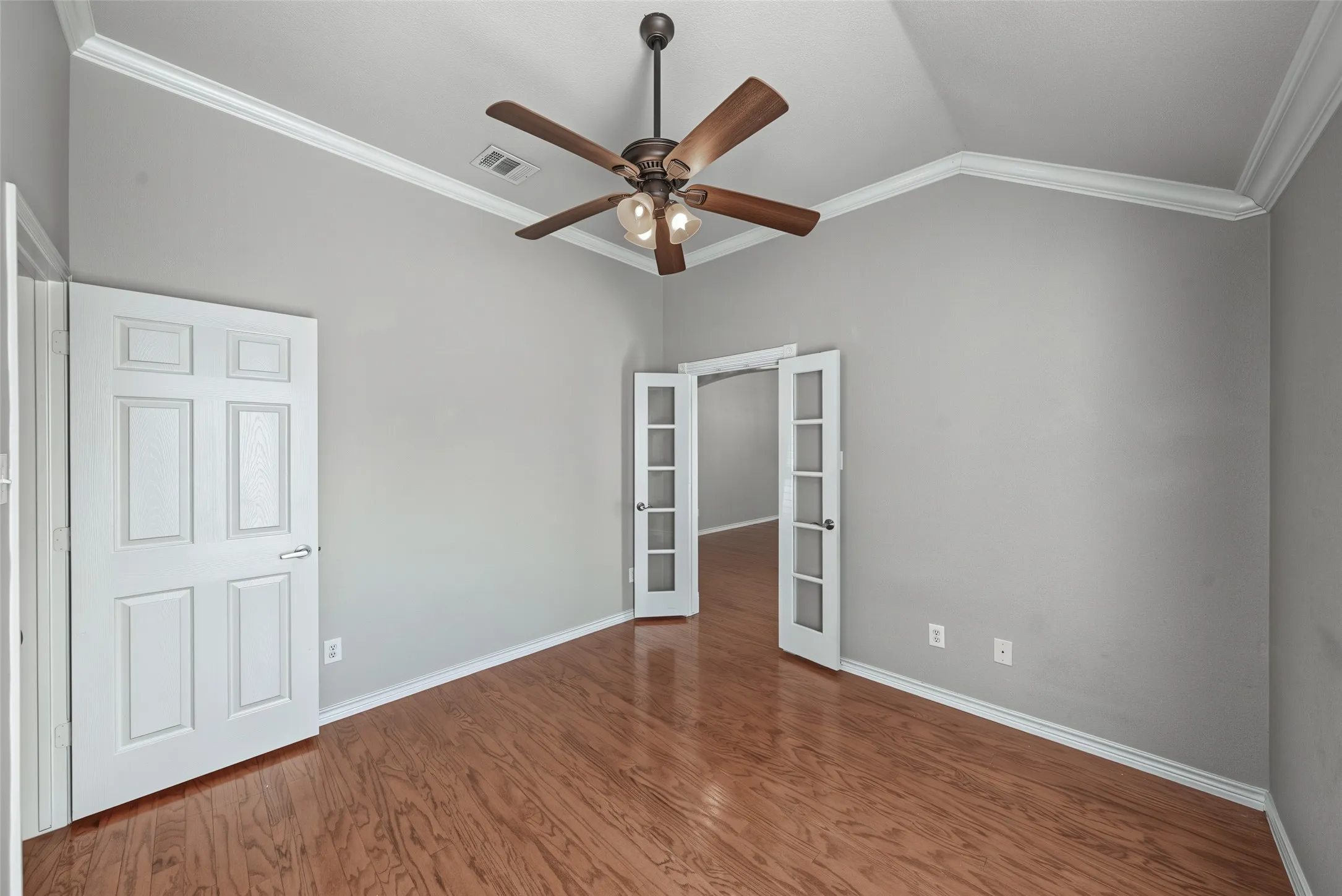 Vaulted ceiling with crown molding, wood-finish flooring, ceiling fan with integrated lighting, and glass-paneled French doors