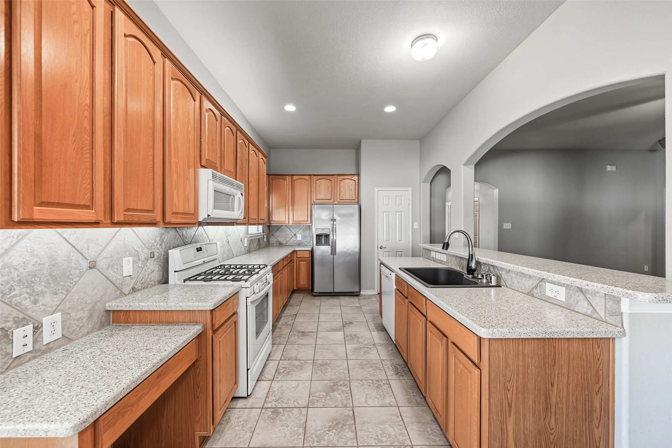 Kitchen featuring wood-finish cabinetry, light-toned countertops, stainless steel refrigerator, white range, and a black single-basin sink with a gooseneck faucet