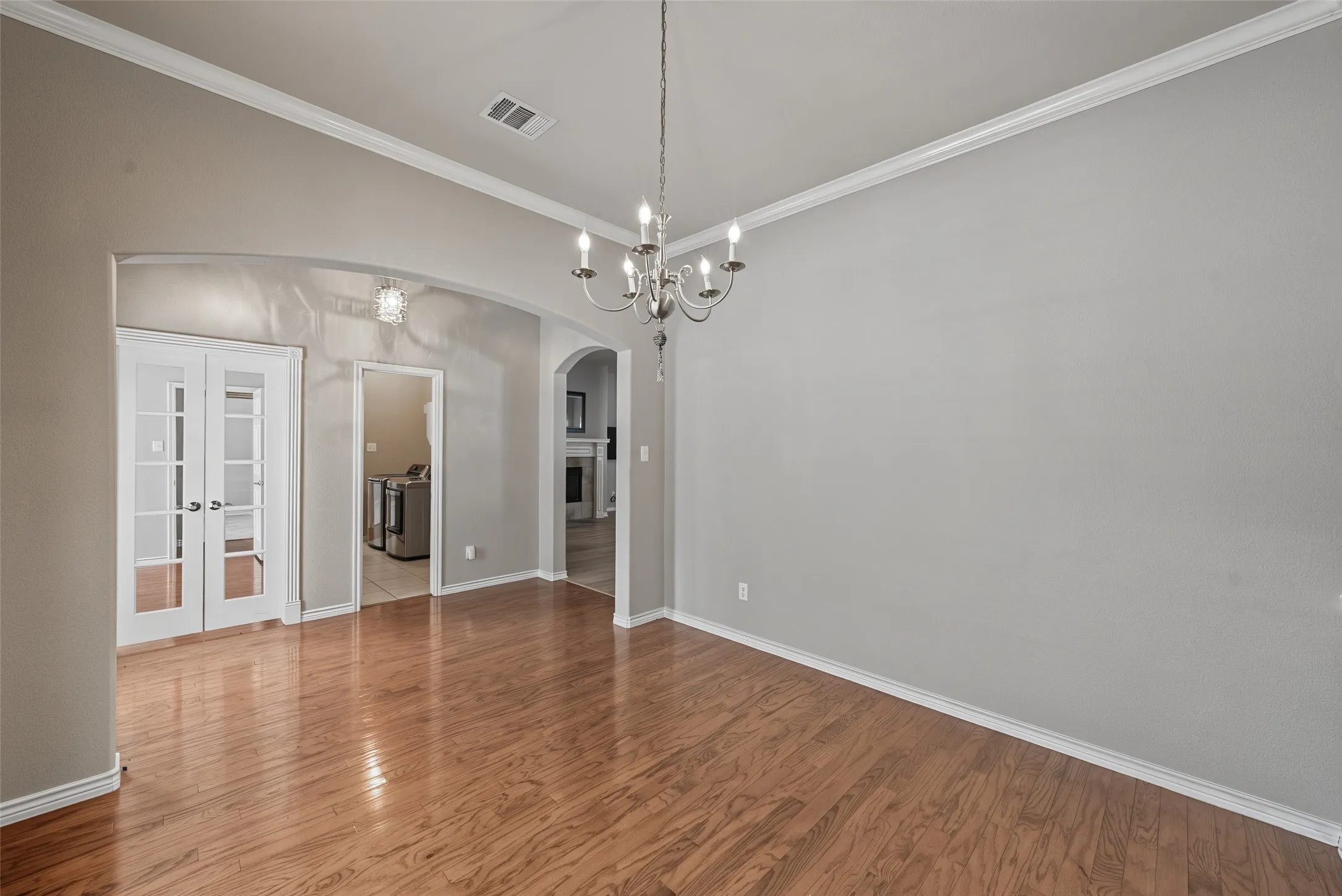 Hardwood flooring, crown molding, arched entryways, chandelier lighting, French doors