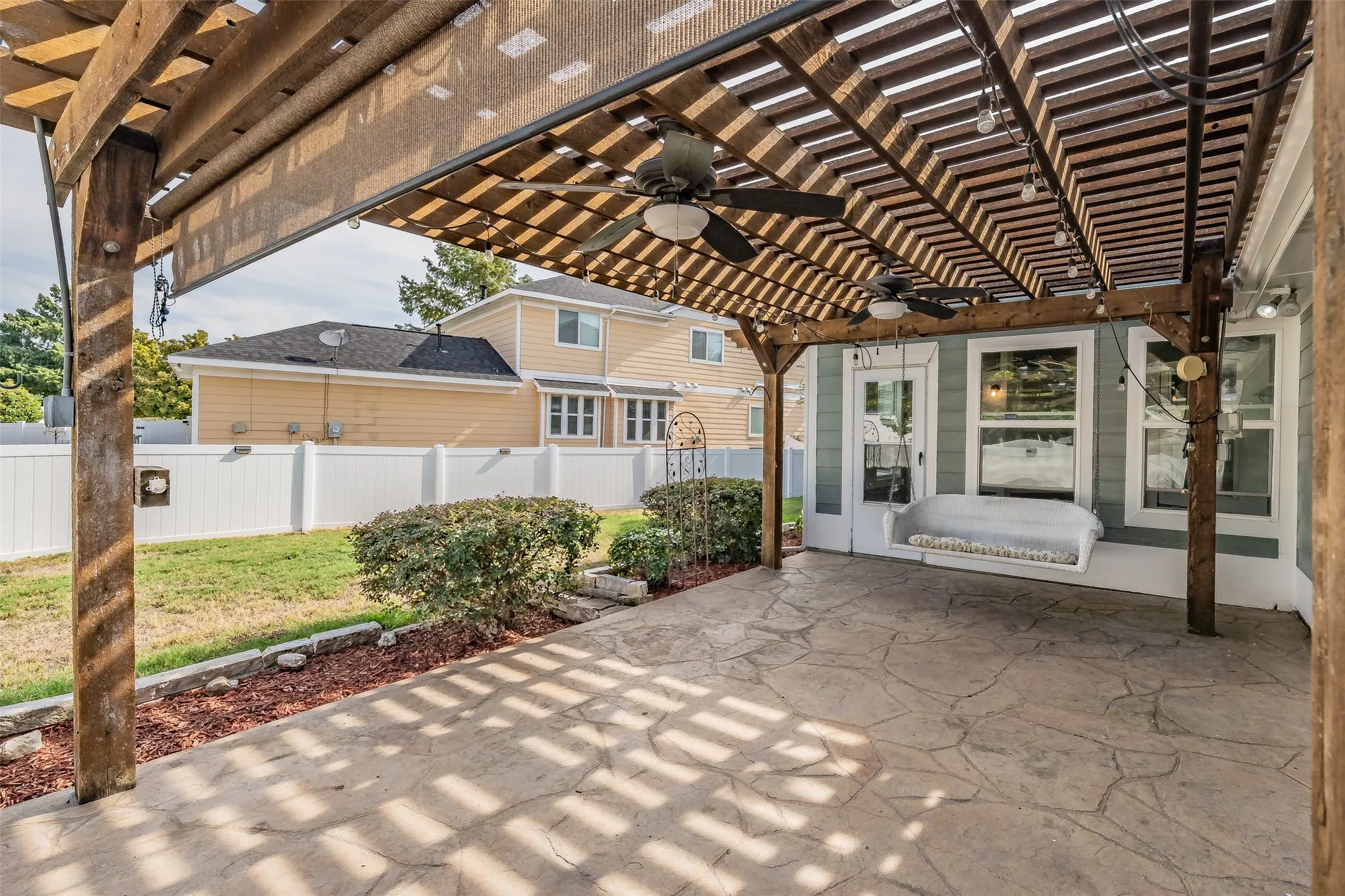 Expansive stamped concrete patio with a wooden pergola, featuring two ceiling fans and integrated string lighting