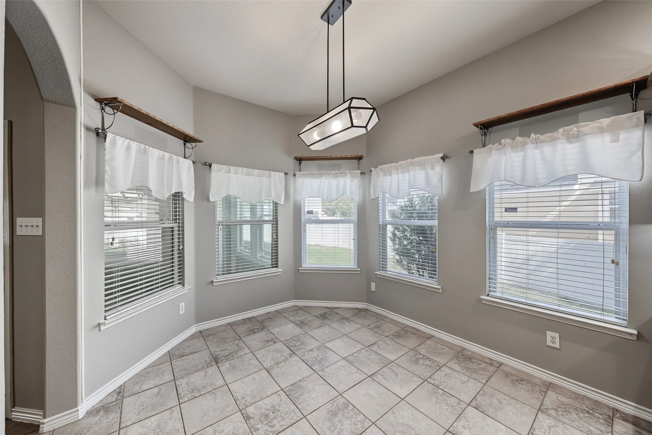 Angled walls with multiple windows, vaulted ceiling, tile flooring, contemporary geometric light fixture, and built-in shelving