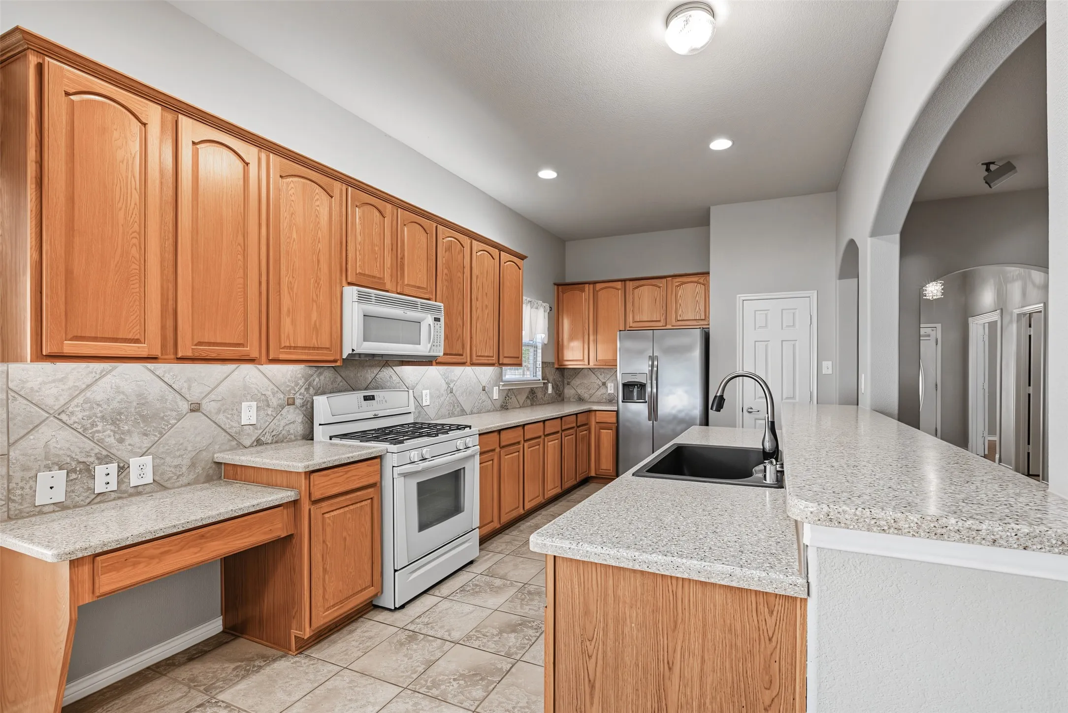 Kitchen featuring warm wood cabinetry, neutral countertops, tiled backsplash, and stainless steel appliances