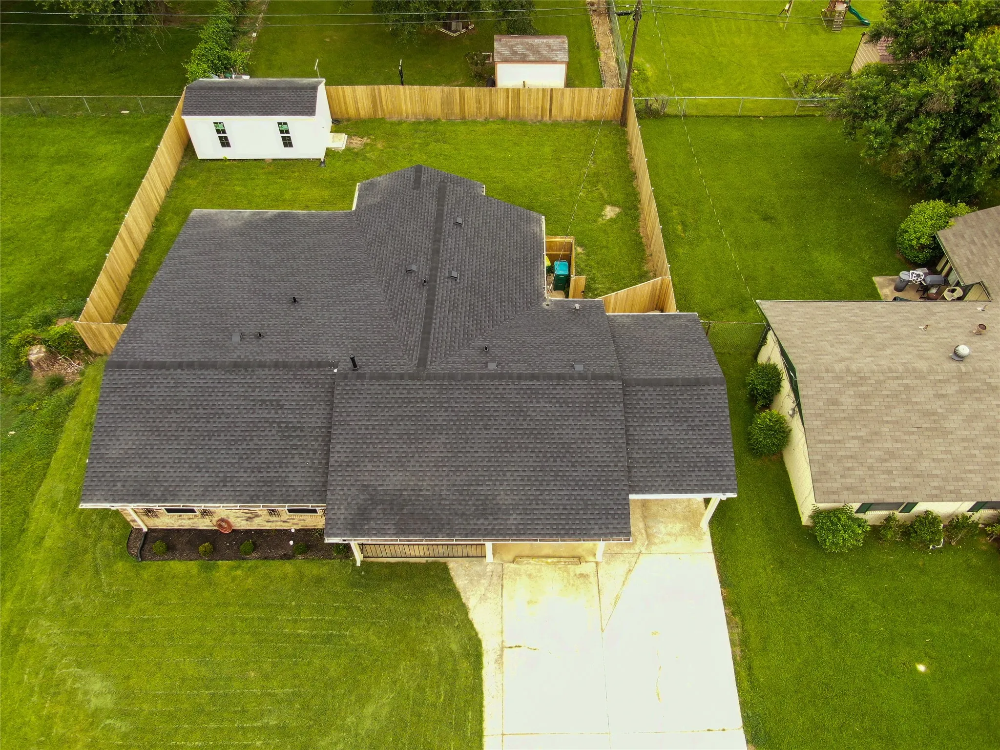 Dark shingle roof, well-maintained lawn, privacy fencing, and an outbuilding