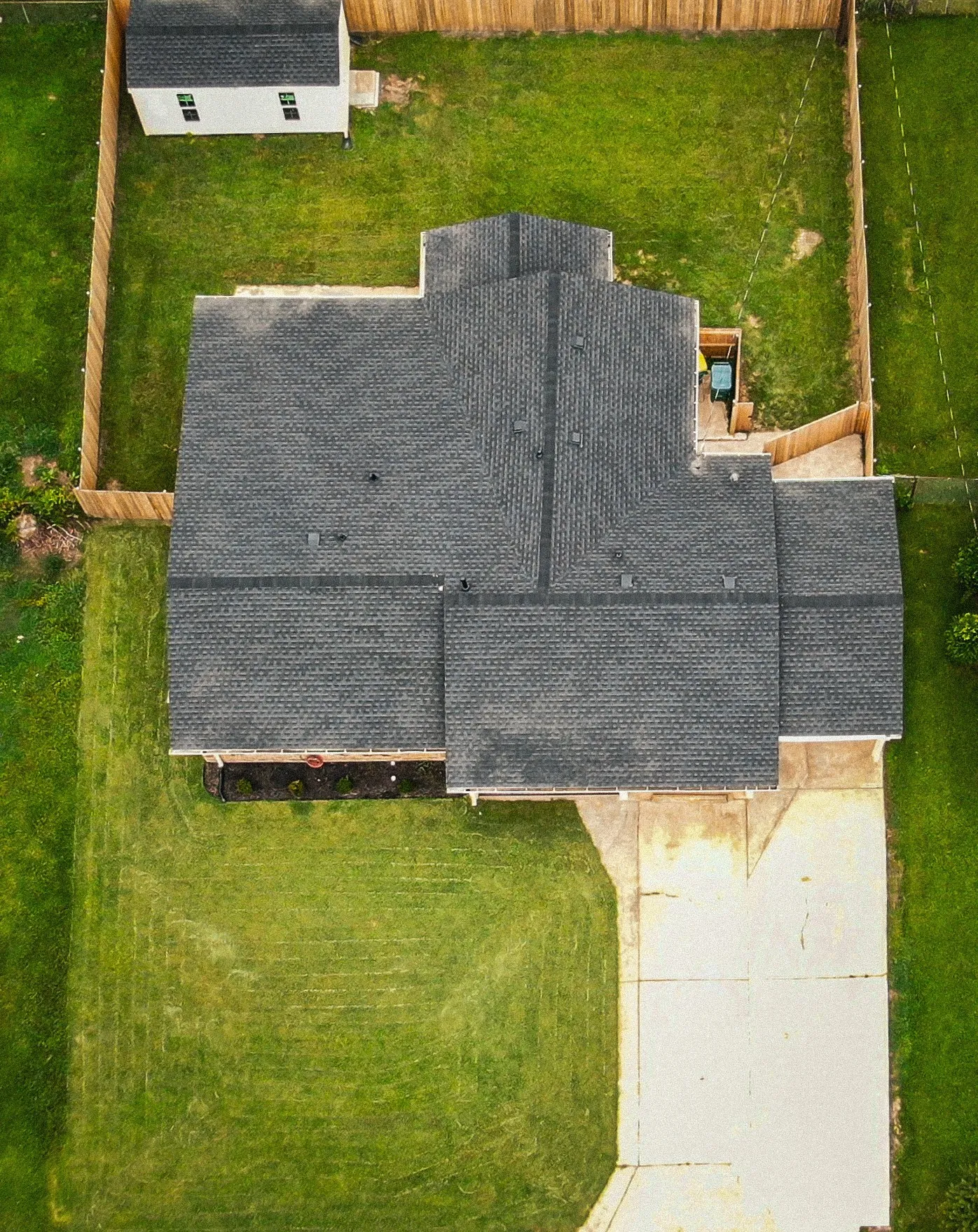 Property featuring a gray shingled roof, a wooden privacy fence, a concrete driveway, a separate storage shed, and a manicured lawn