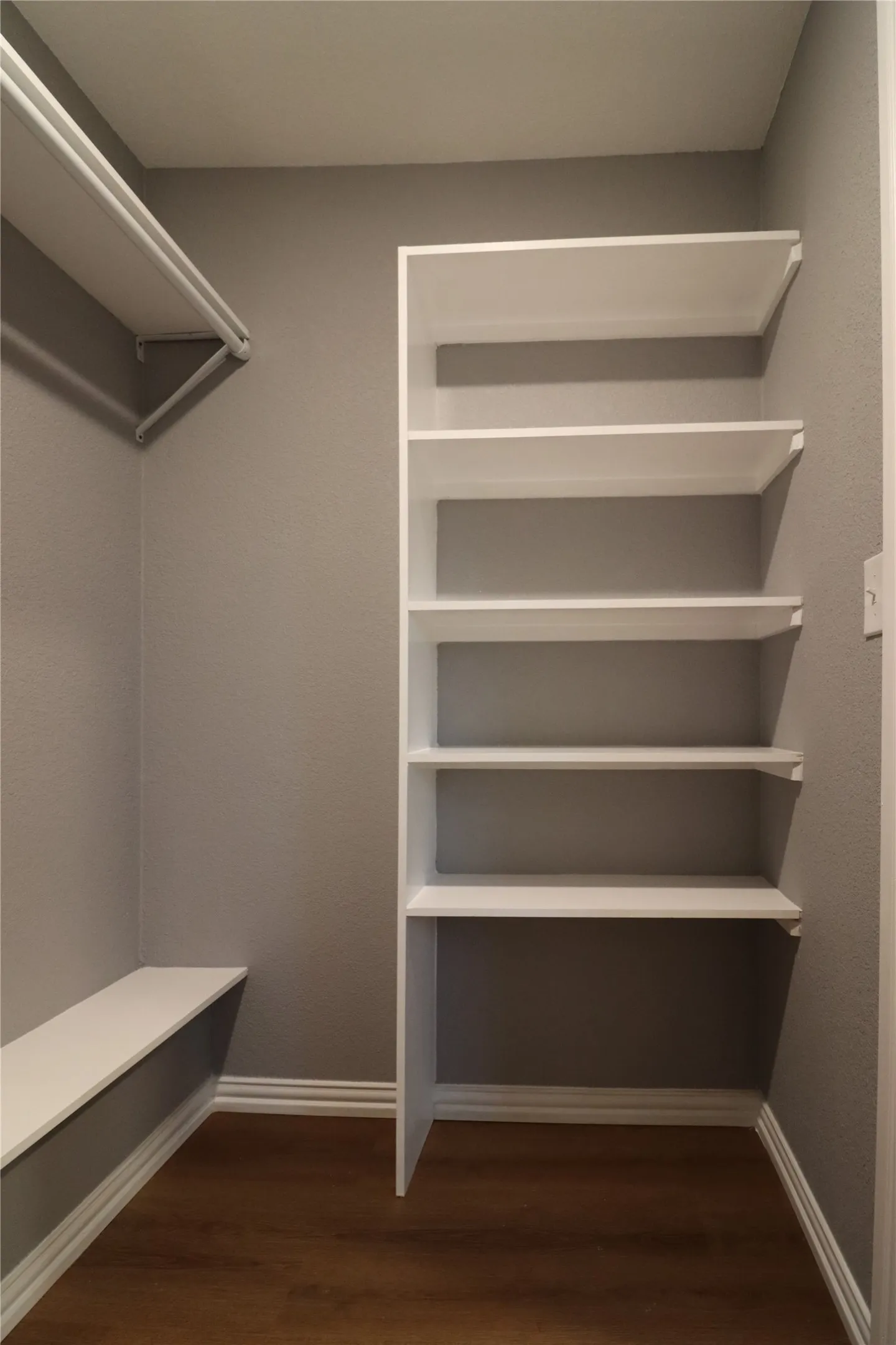 Built-in shelving, integrated clothes rod, wood-finish flooring, white trim, and a built-in bench