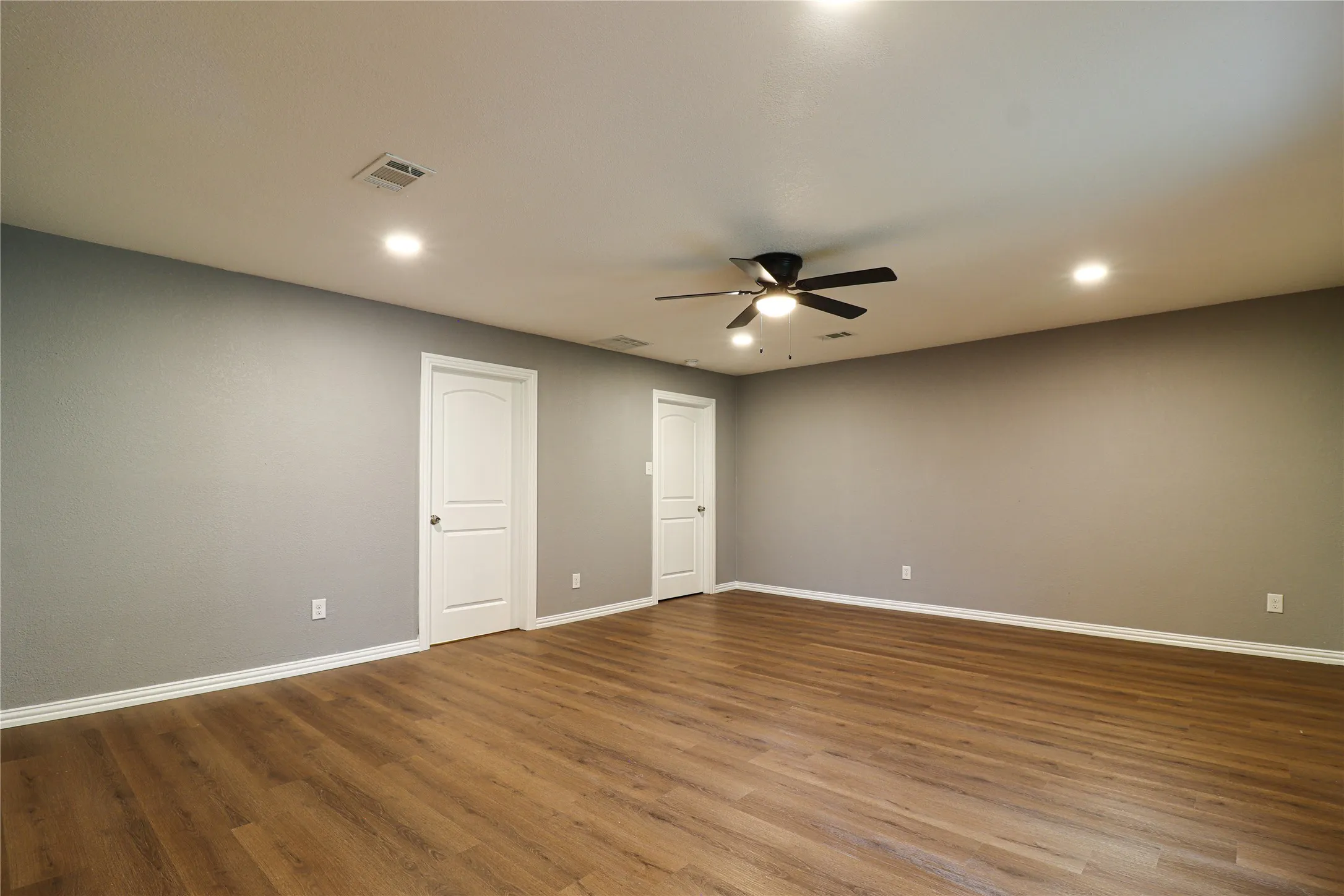 Expansive room with wood-finish flooring, recessed lighting, ceiling fan, and light gray walls