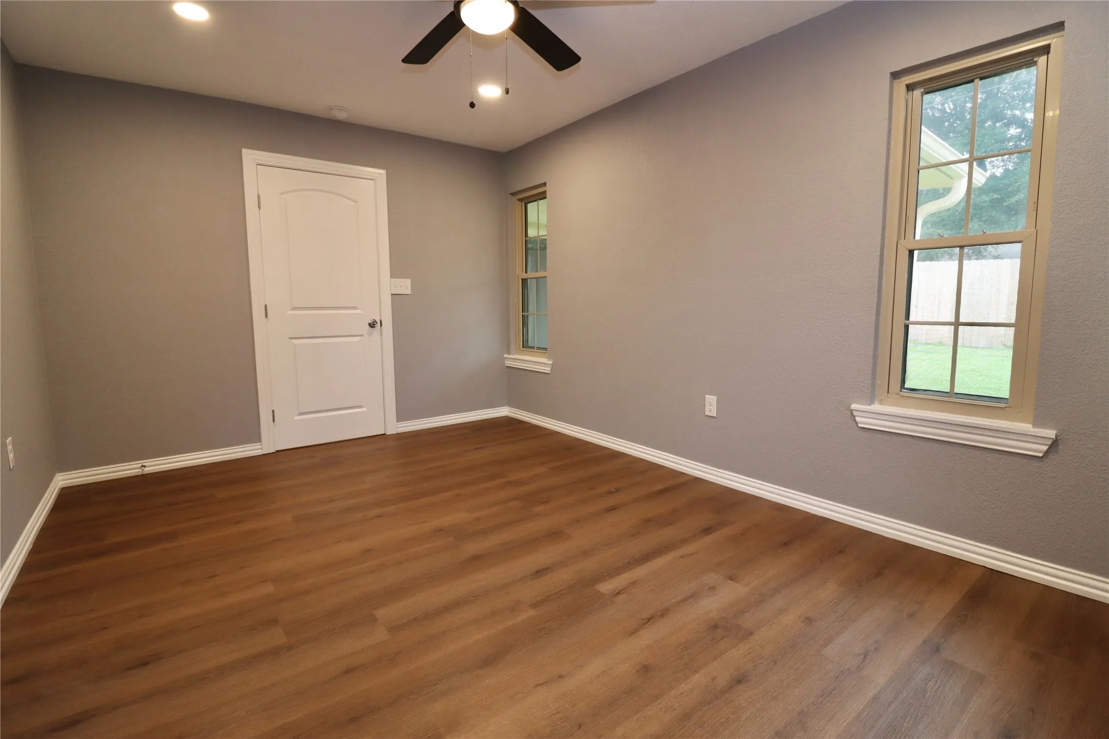 Wood-finish flooring with crisp white trim, neutral gray walls, recessed lighting, and a ceiling fan