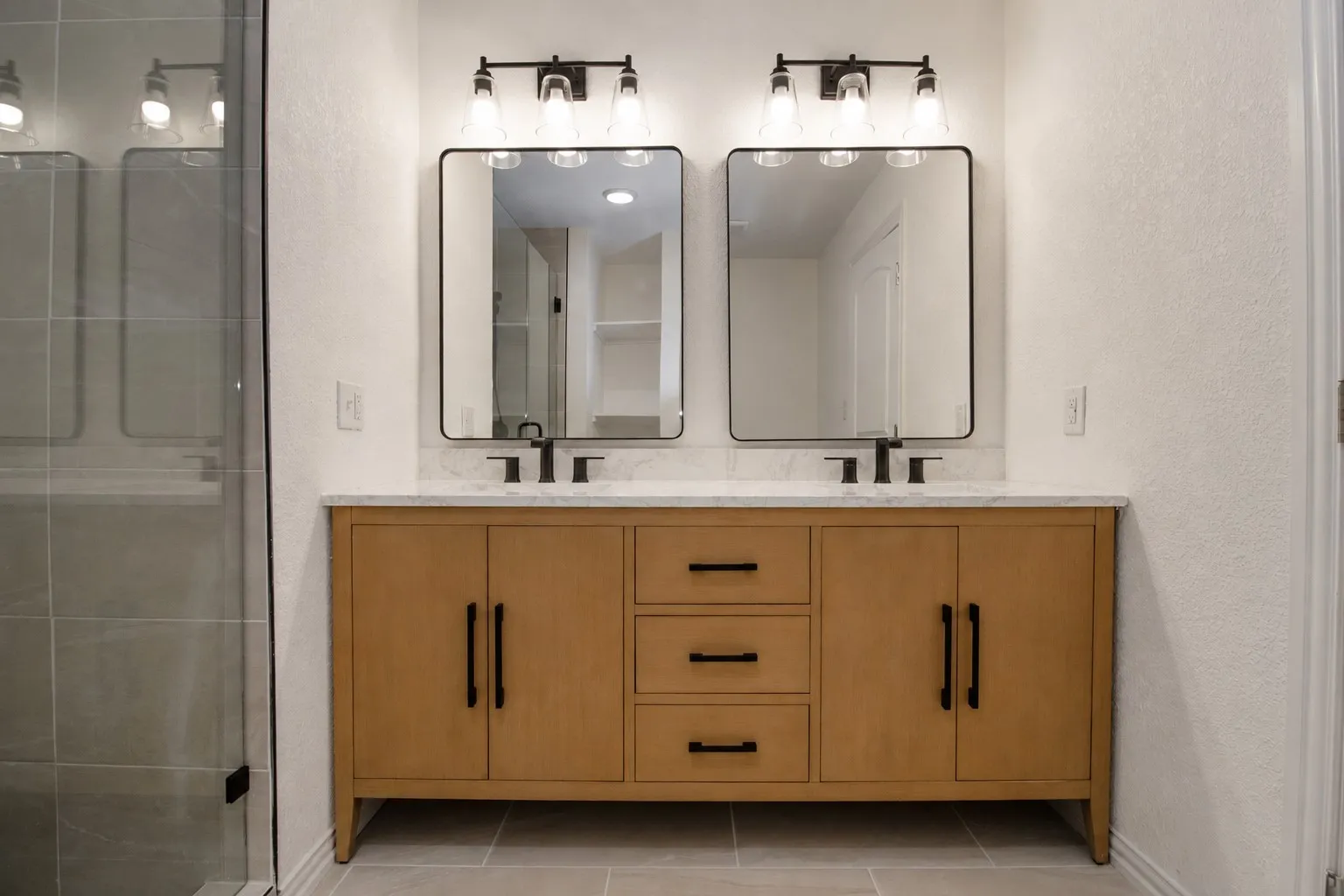 Double vanity with wood-finish cabinetry, black hardware, and two framed mirrors