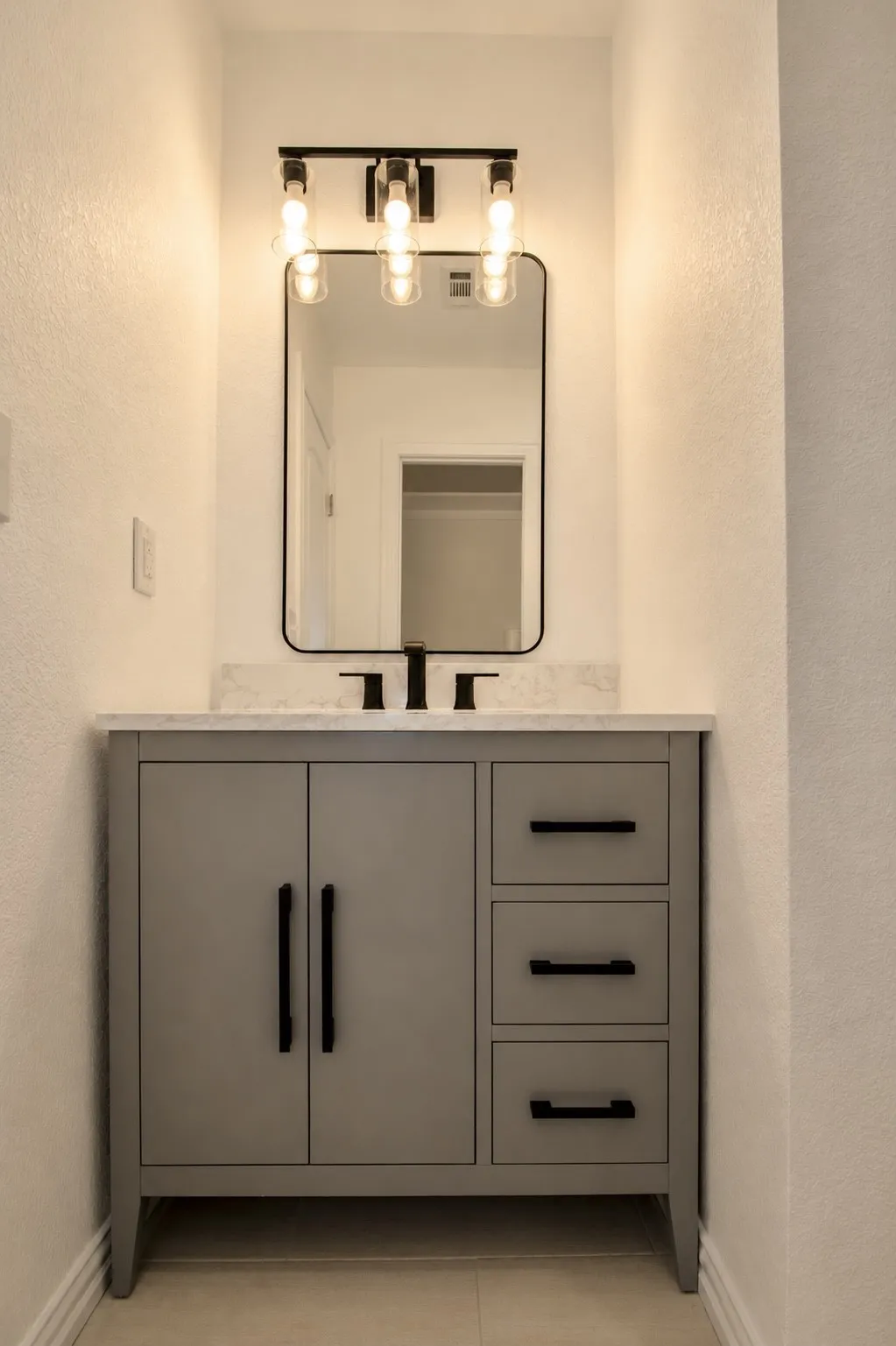 Gray vanity with matte black hardware, white countertop, and rectangular framed mirror