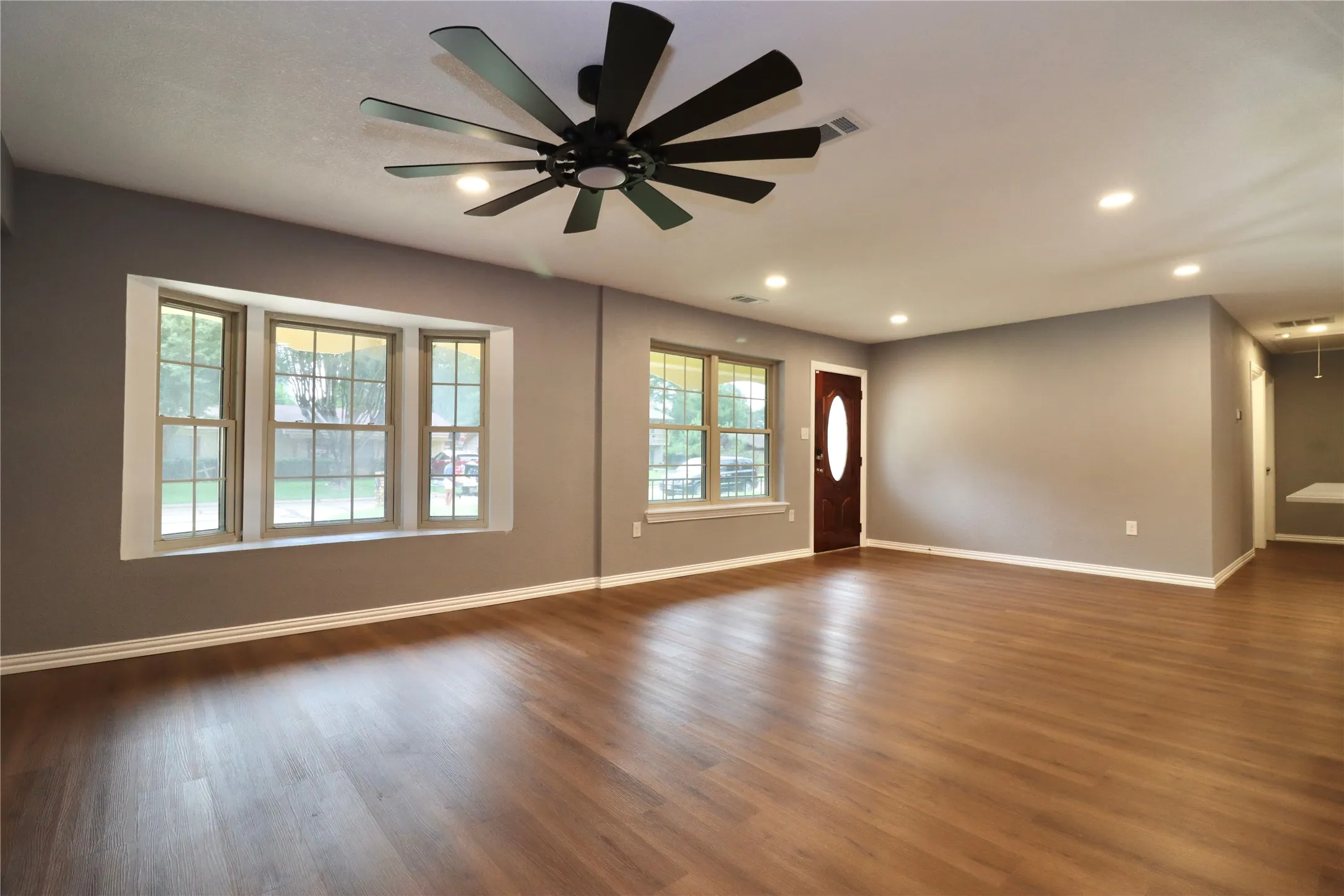 Wood-finish flooring, recessed lighting, bay window, ceiling fan, and a wood-paneled entry door