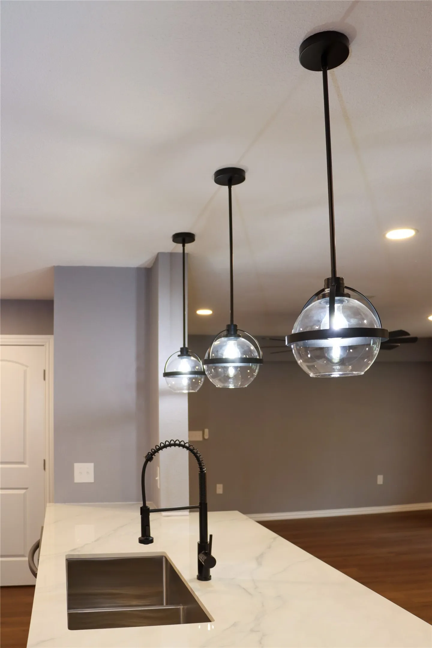 White countertop with gray veining, black gooseneck faucet, undermount sink, and three pendant lights with spherical glass globes