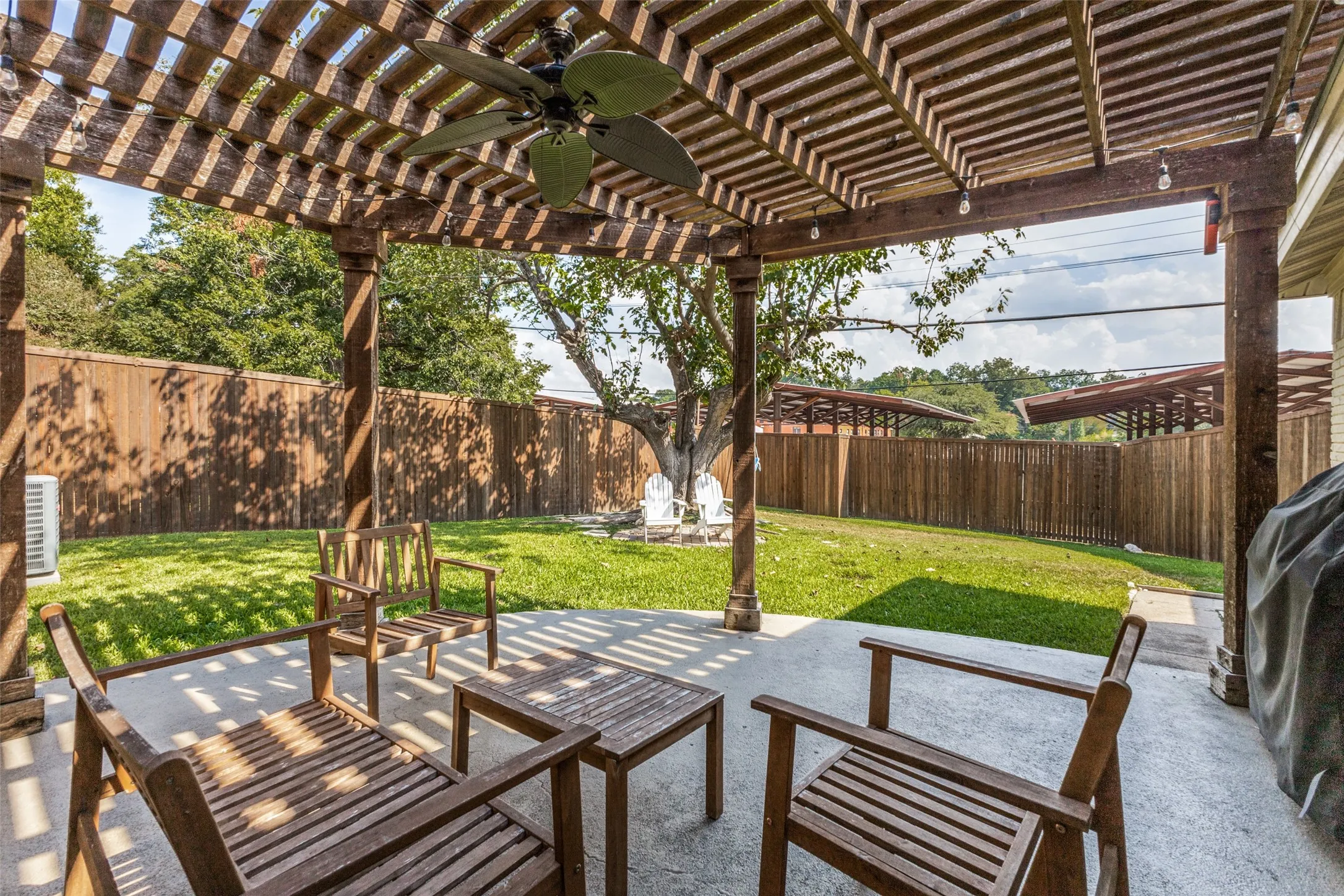 Expansive outdoor patio with a wooden pergola, ceiling fan, and string lighting