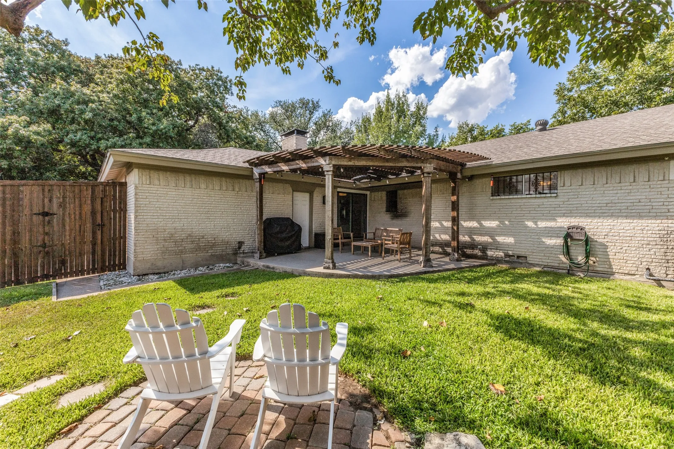 Expansive backyard featuring a manicured lawn, brick paver patio, wood pergola, and full privacy fencing