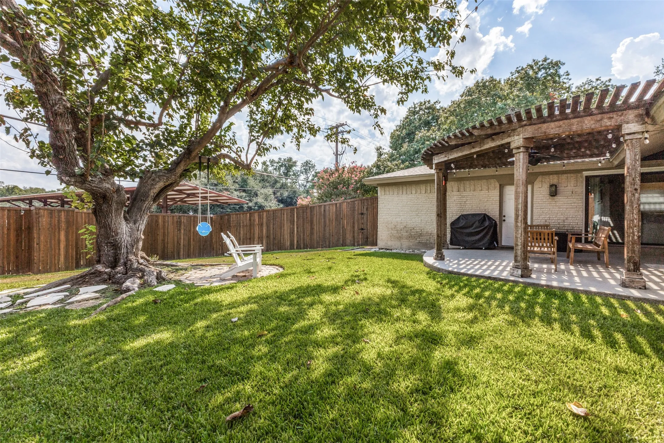 Expansive backyard featuring a pergola-covered patio, mature shade tree, and wood privacy fencing