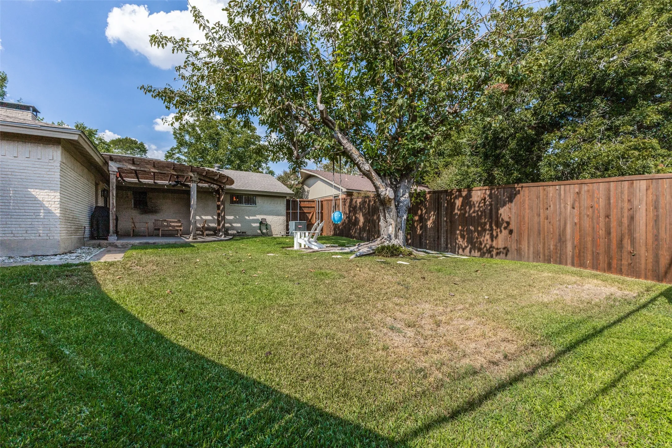 Expansive backyard with a manicured lawn, established tree, and a solid wood fence