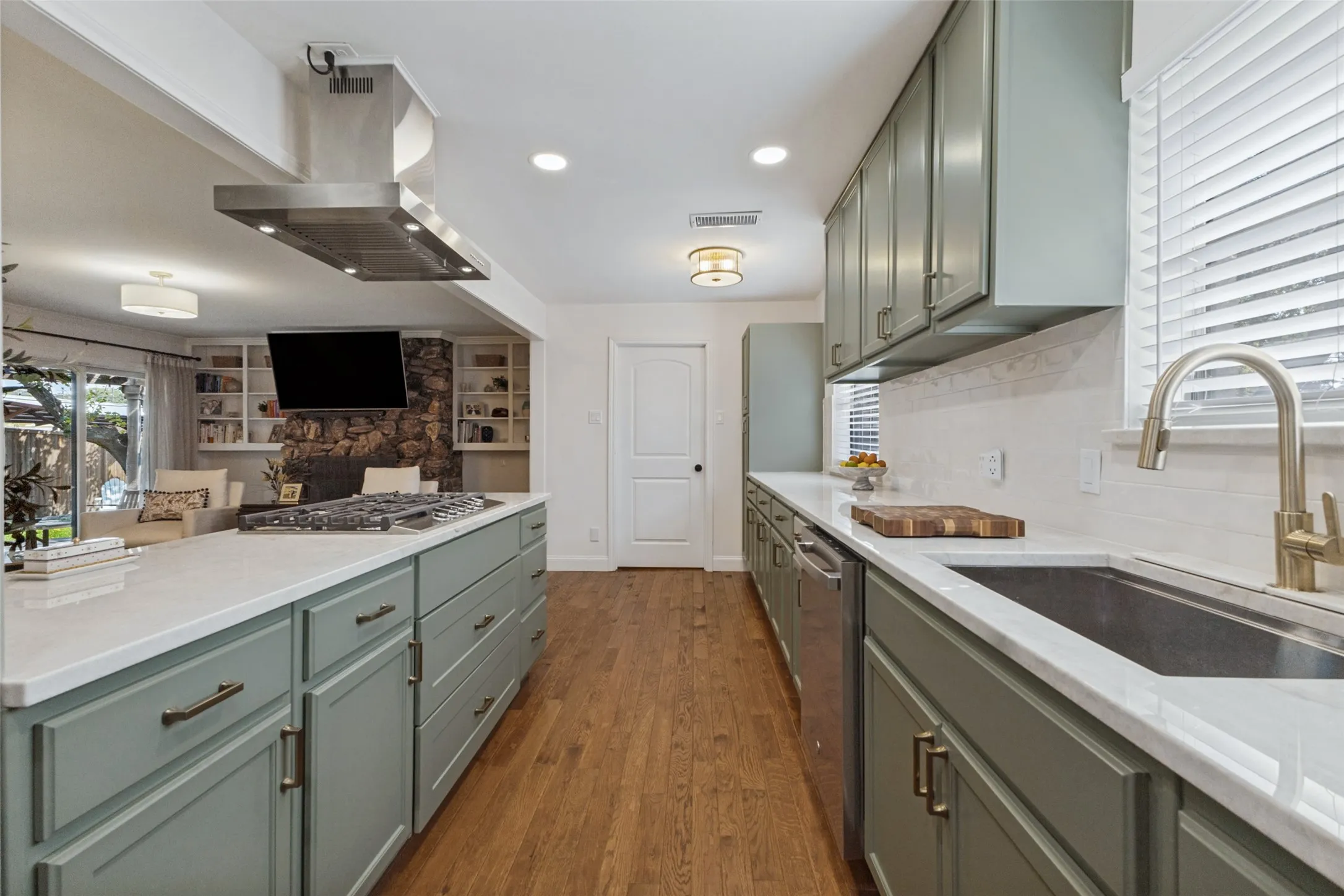 Kitchen featuring an expansive island with cooktop, stainless steel range hood, full-height backsplash, wood-finish flooring, and recessed lighting