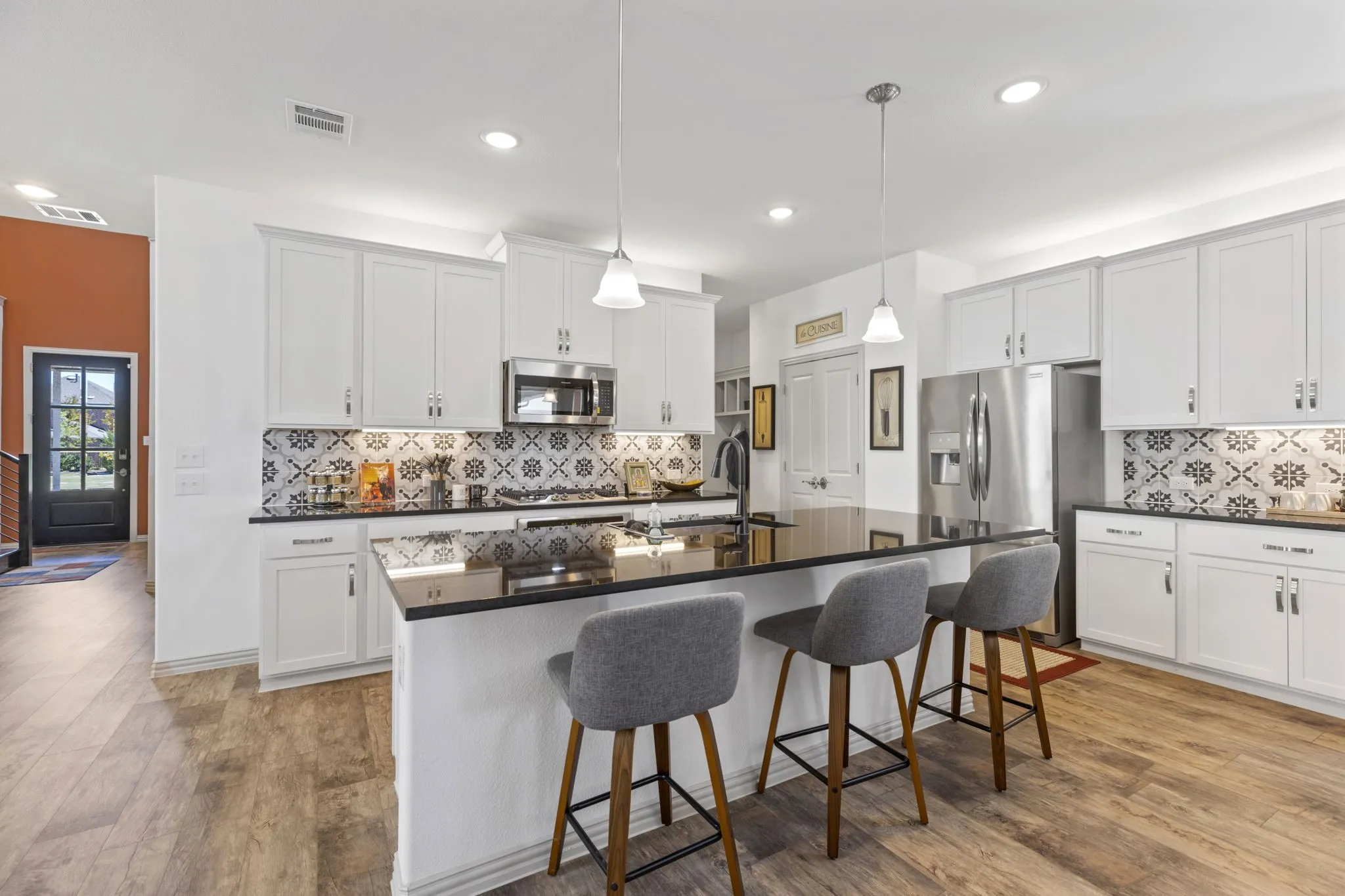 Kitchen featuring a large island with dark countertops, white cabinetry, decorative tile backsplash, stainless steel appliances, and wood-finish flooring