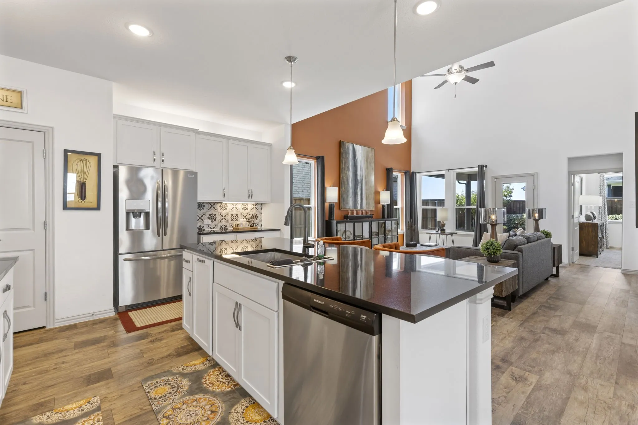 Open-concept kitchen featuring an island with a sink, stainless steel appliances, and wood-finish flooring